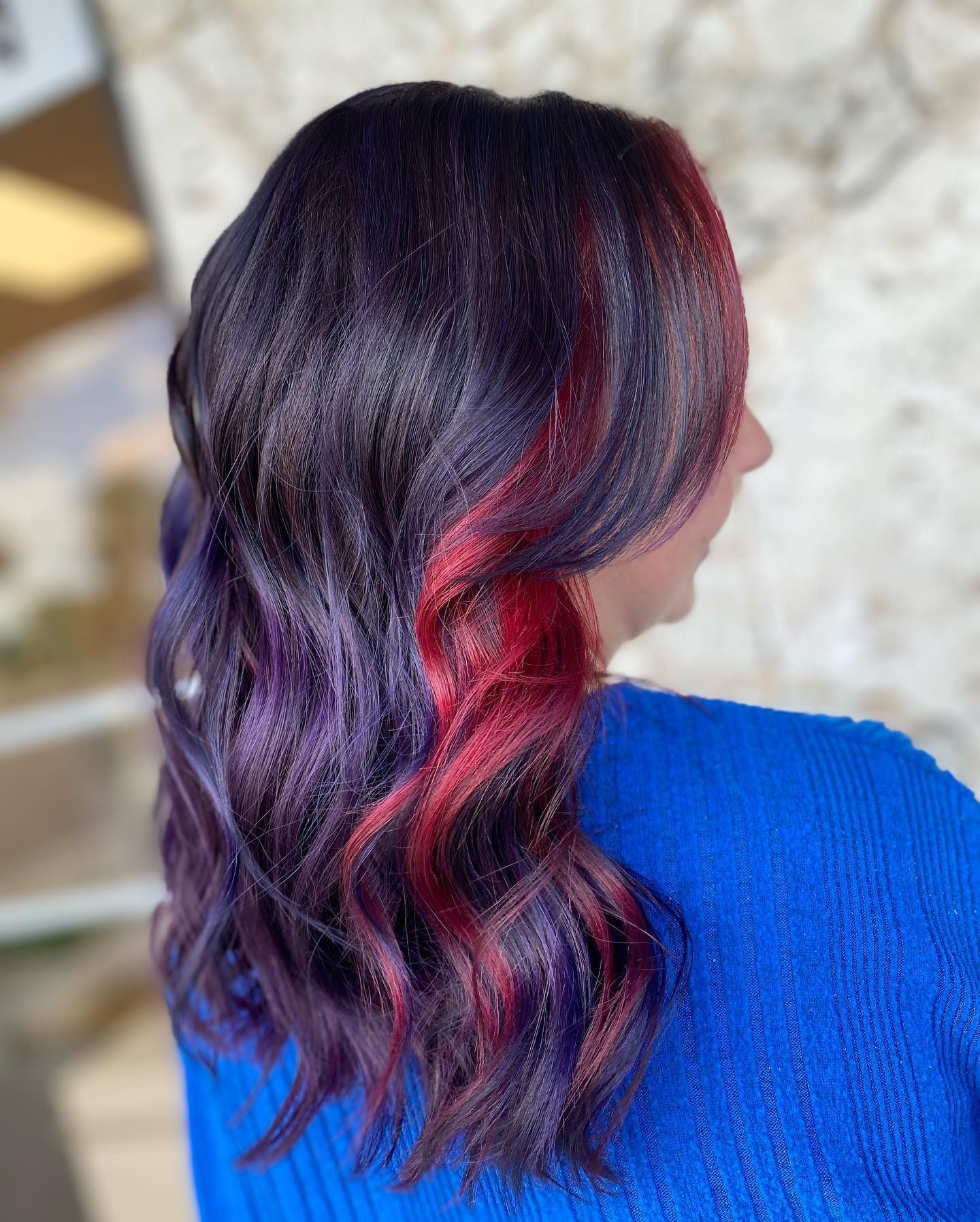 A woman with purple and red hair is wearing a blue sweater.