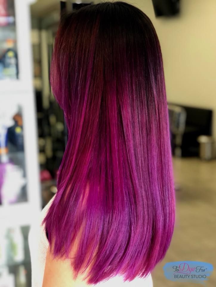 A woman with long purple hair is wearing a white shirt.