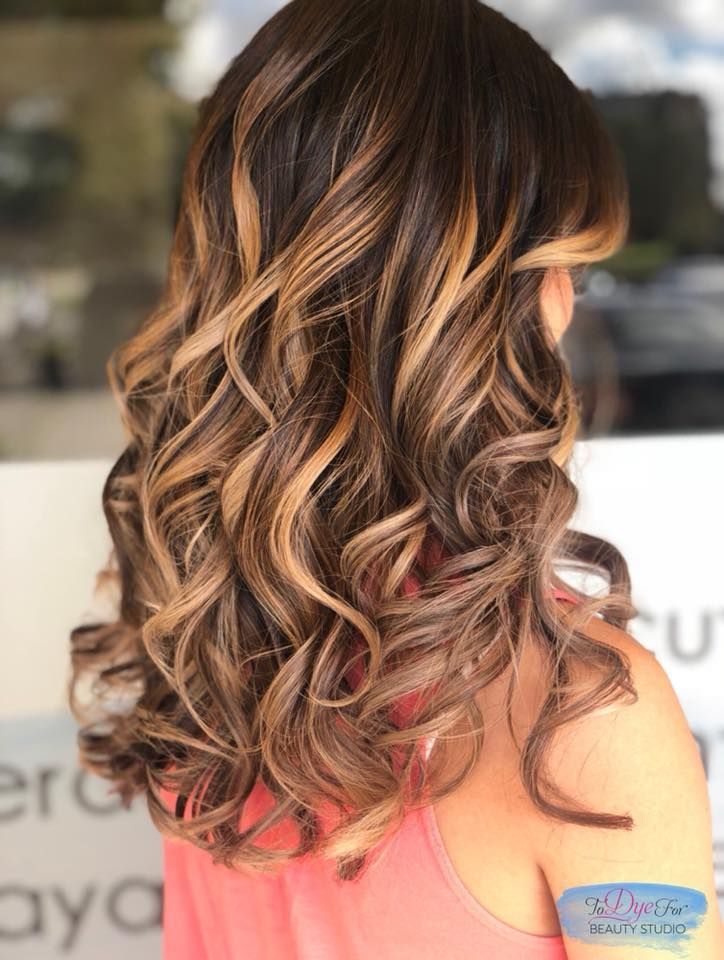 A woman with long curly hair is wearing a pink tank top.