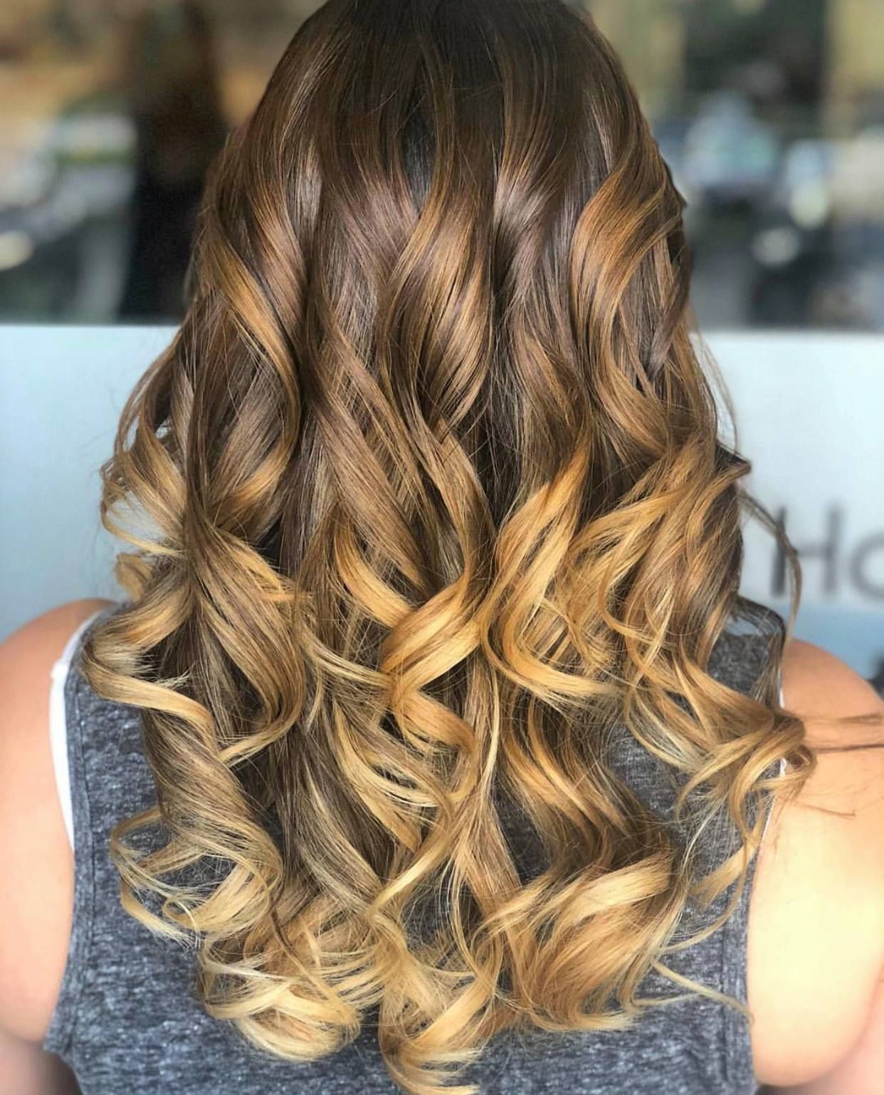 A woman with long curly hair is wearing a gray tank top.