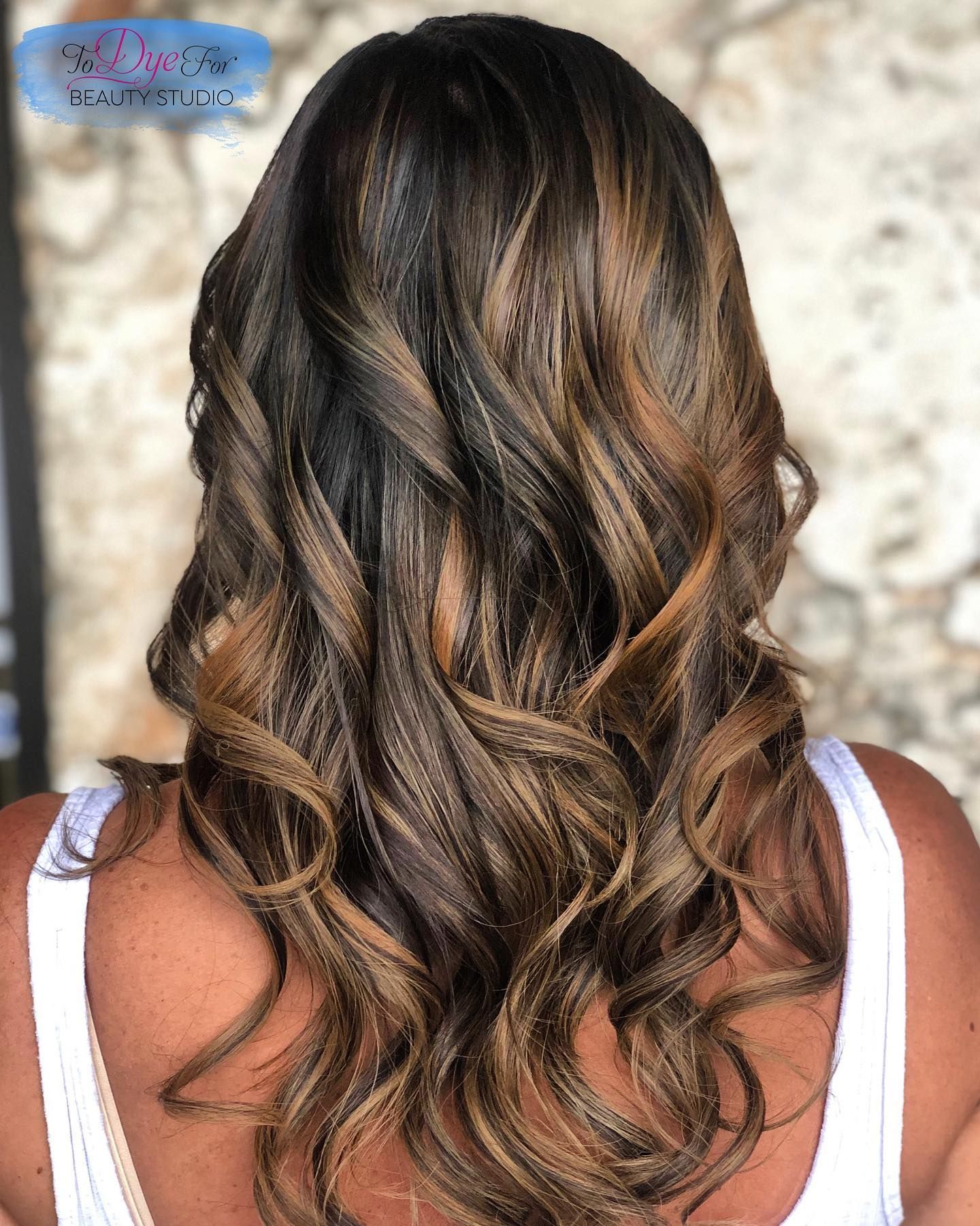 A woman with long brown hair is wearing a white tank top.