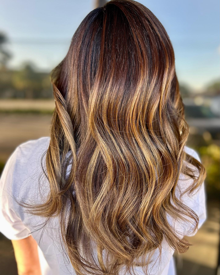 A woman with long brown hair and blonde highlights is wearing a white shirt.