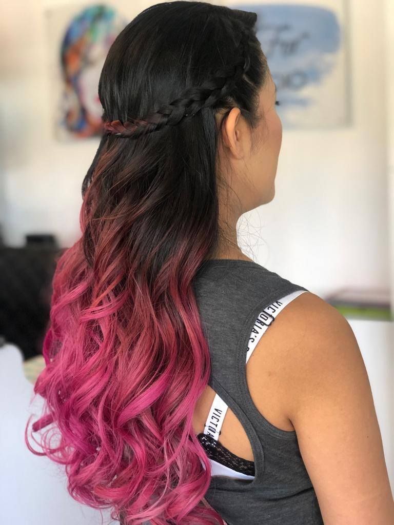 A woman with long pink hair is wearing a braided half up half down hairstyle.