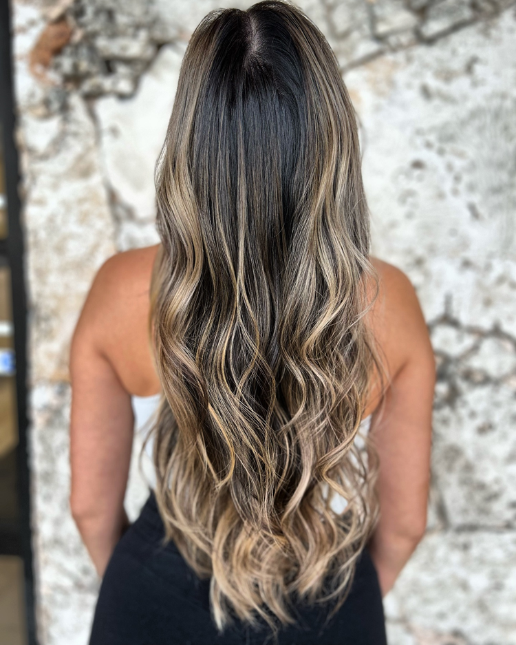 A woman with long hair is standing in front of a stone wall.