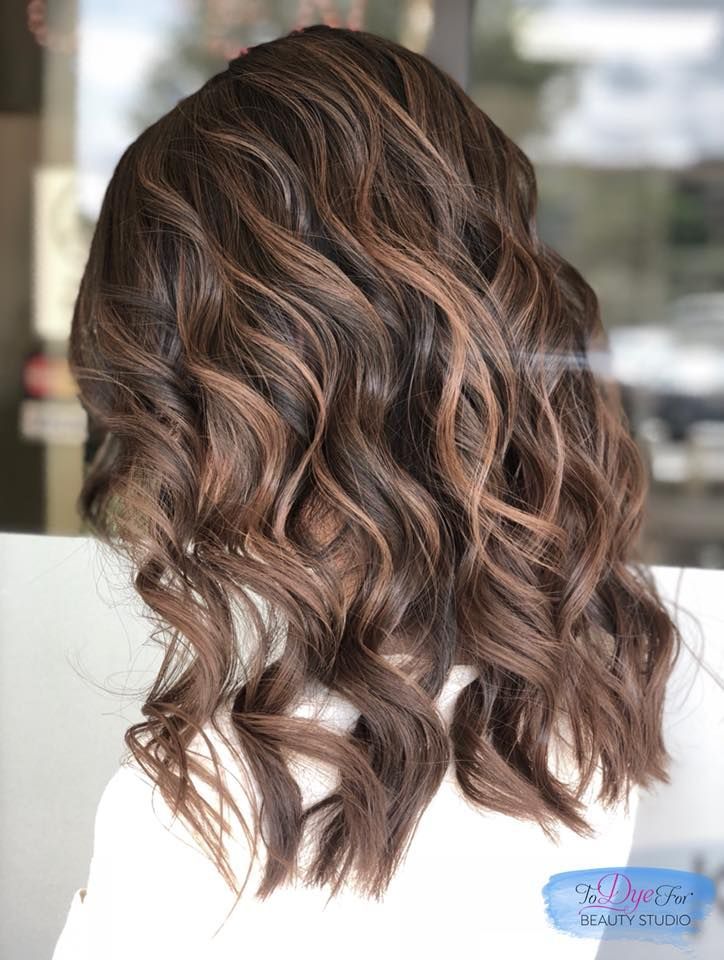 A woman with long brown wavy hair is wearing a white shirt.