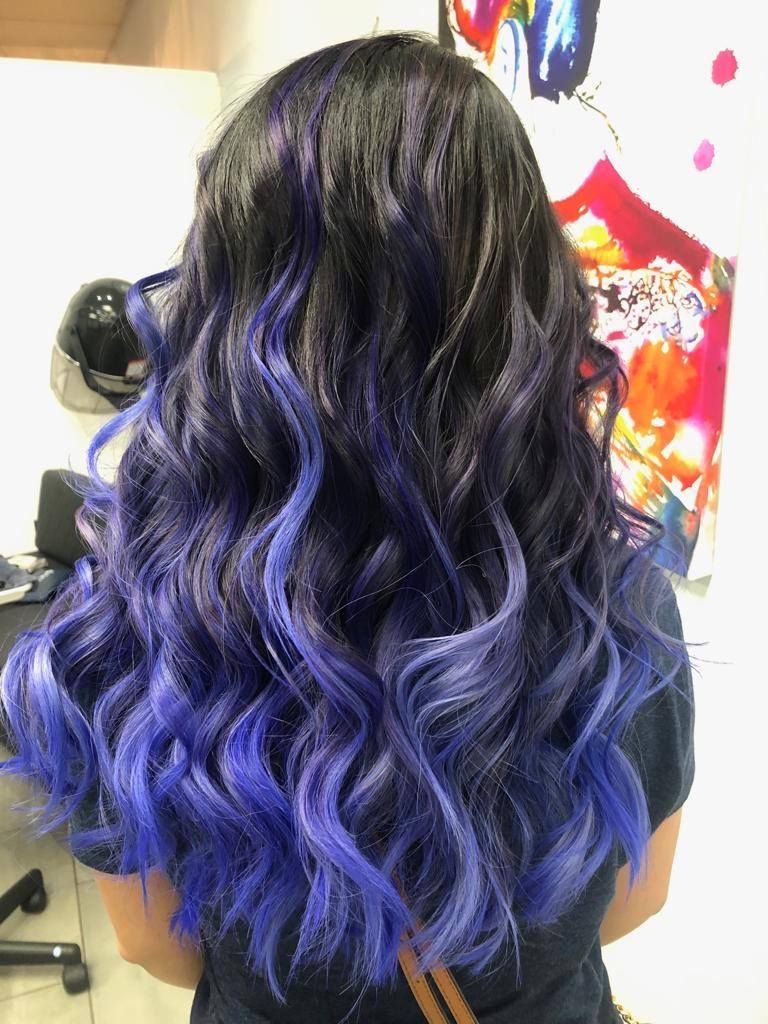 A woman with purple hair is standing in front of a wall.