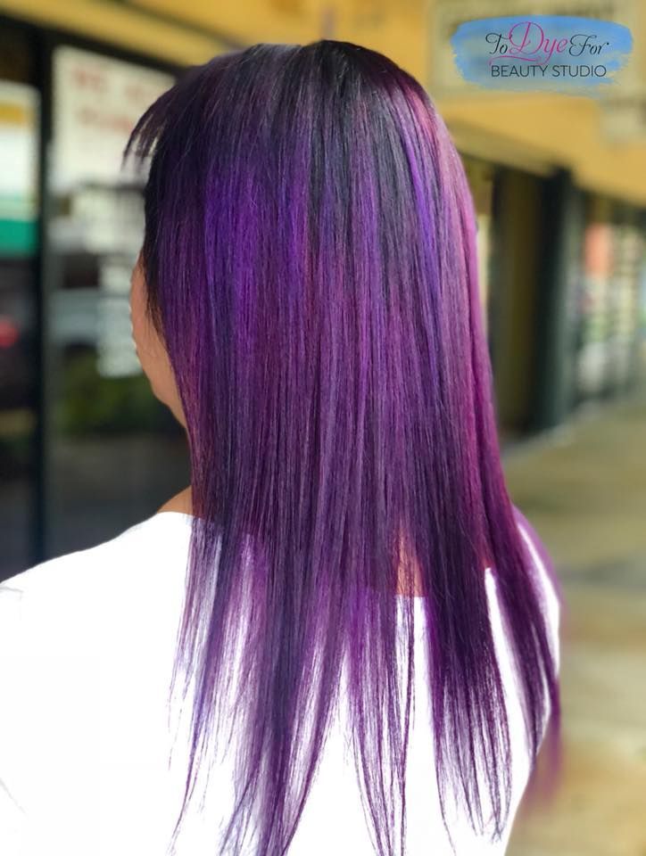 A woman with long purple hair is wearing a white shirt.