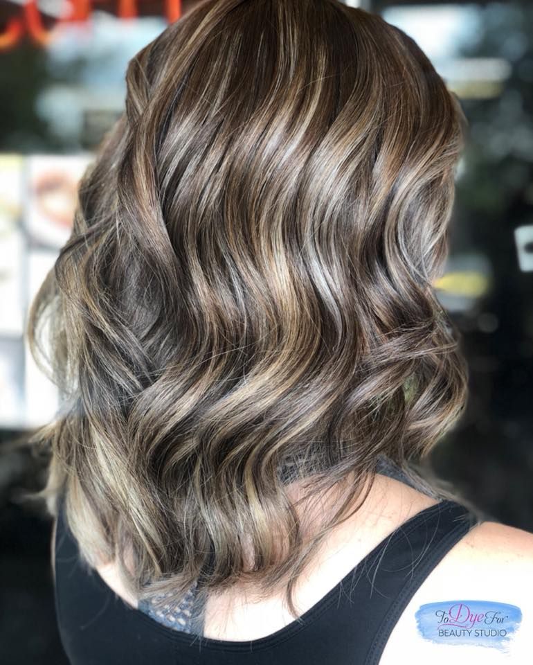 A woman with long wavy brown hair is wearing a black tank top.