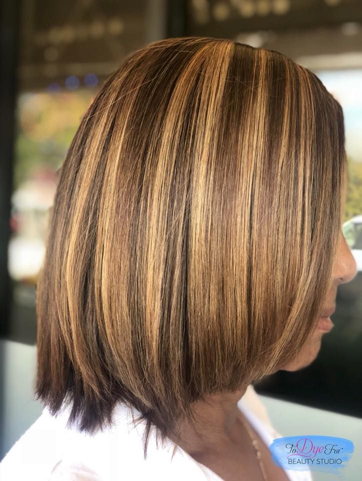 A woman with brown hair and blonde highlights is wearing a white shirt.