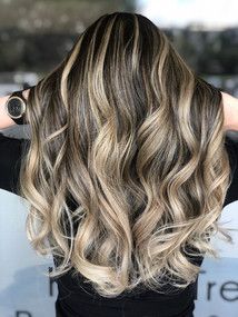 A woman with long wavy hair is wearing a black shirt and a watch.