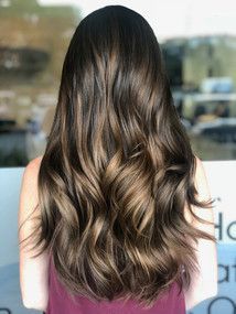 A woman with long brown hair is standing in front of a window.