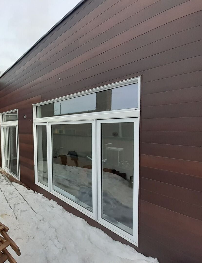 Une maison avec beaucoup de fenêtres et beaucoup de neige au sol.