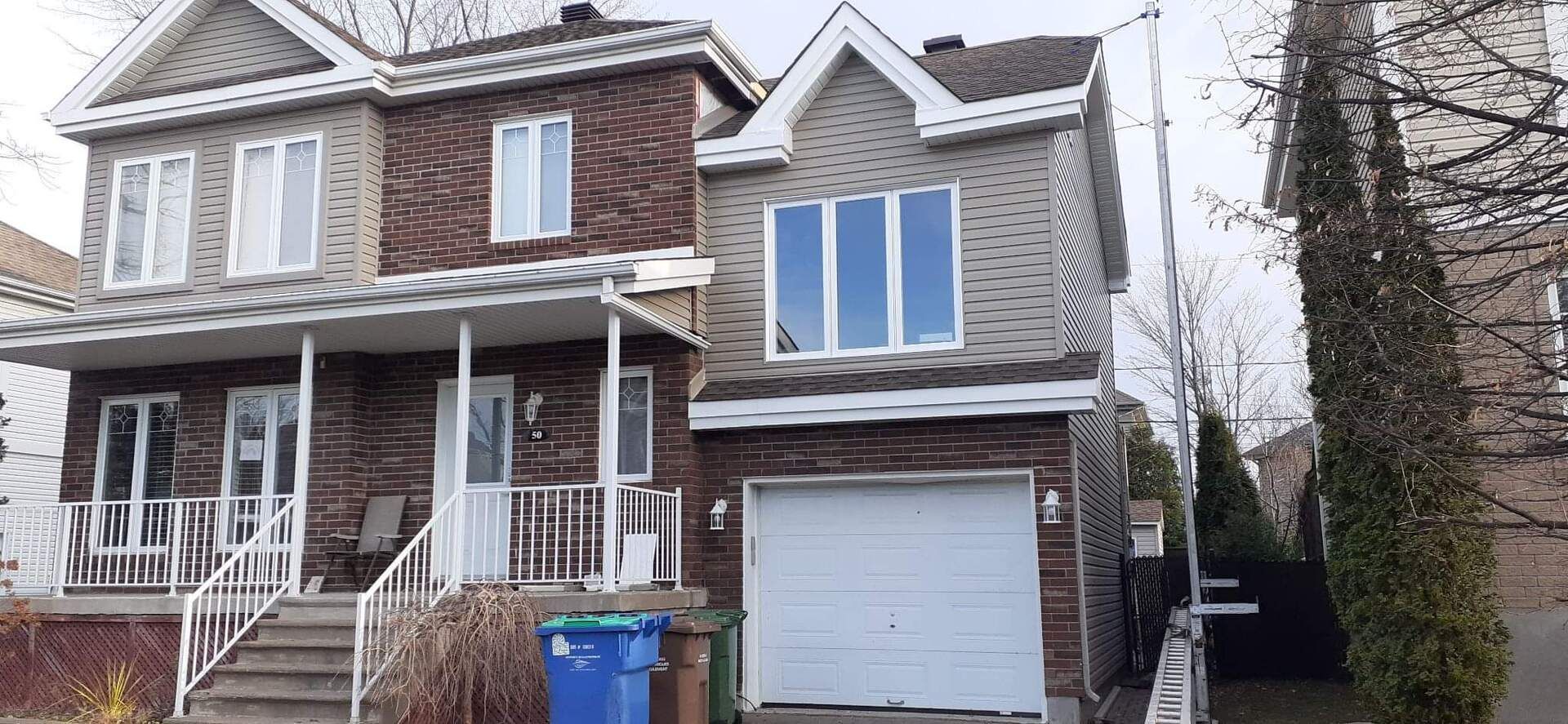 Une maison en briques avec une porte de garage blanche et une poubelle bleue devant.