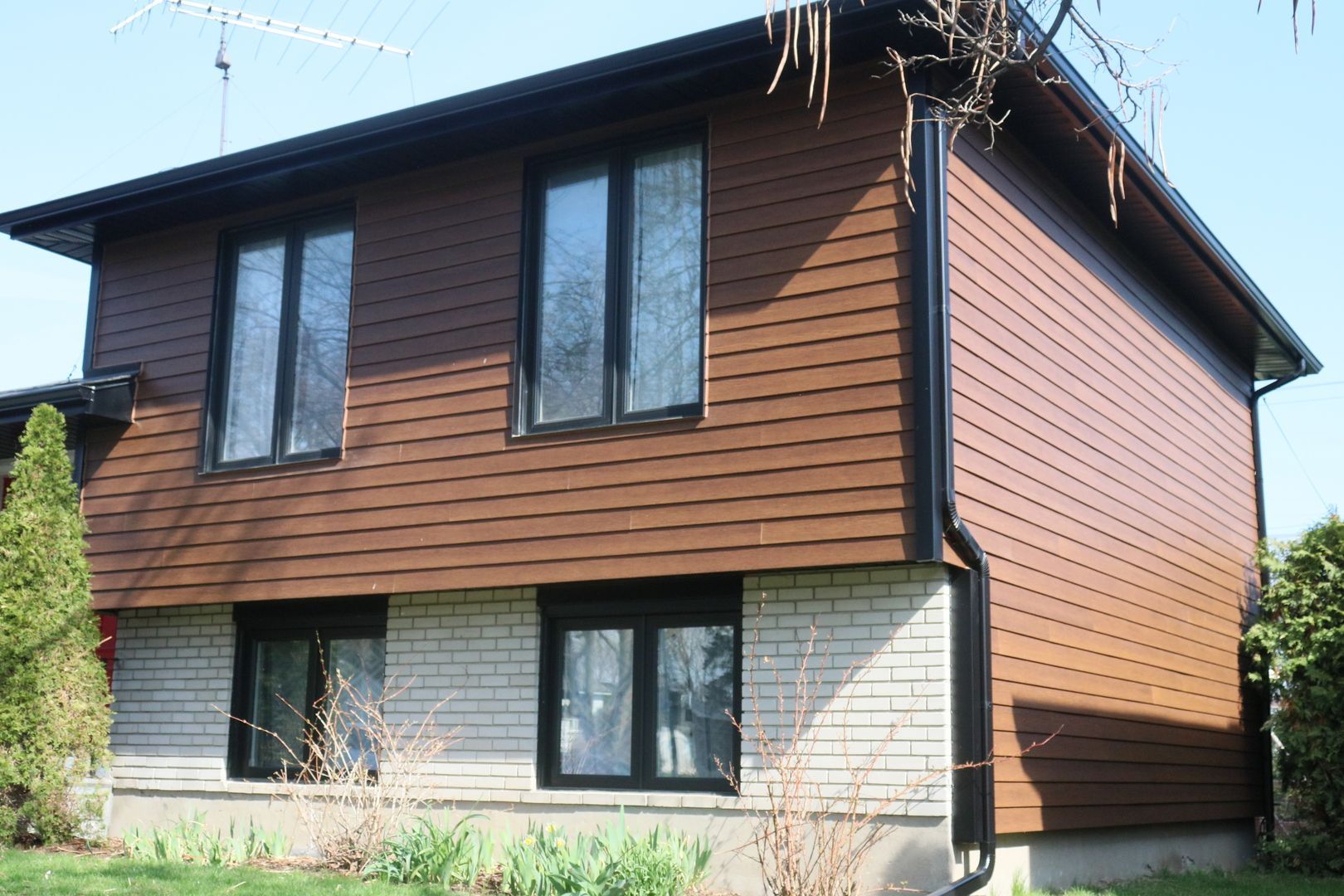 Une maison avec un revêtement marron et des fenêtres noires