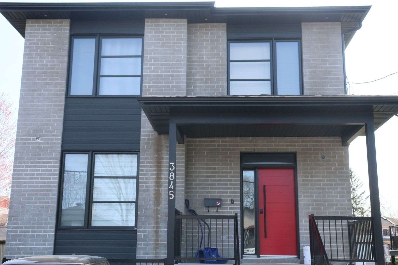 Une maison en briques avec une porte rouge et des fenêtres noires
