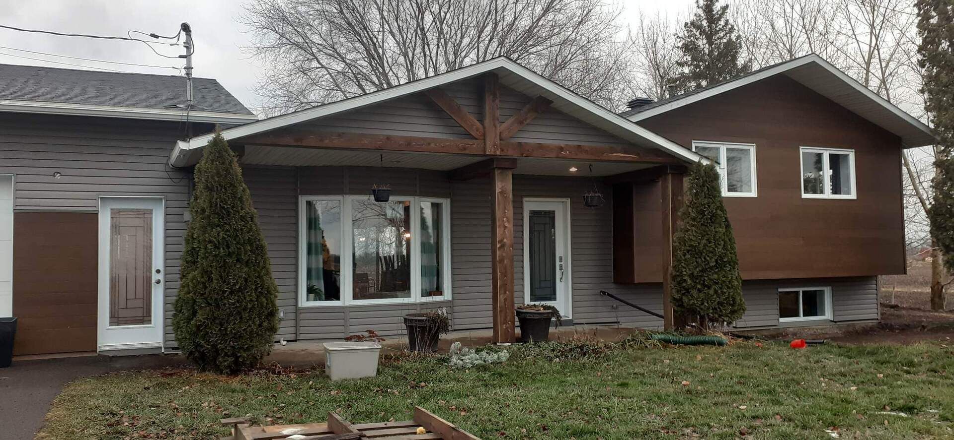 Une maison avec un porche et un garage est située au sommet d'un champ verdoyant.
