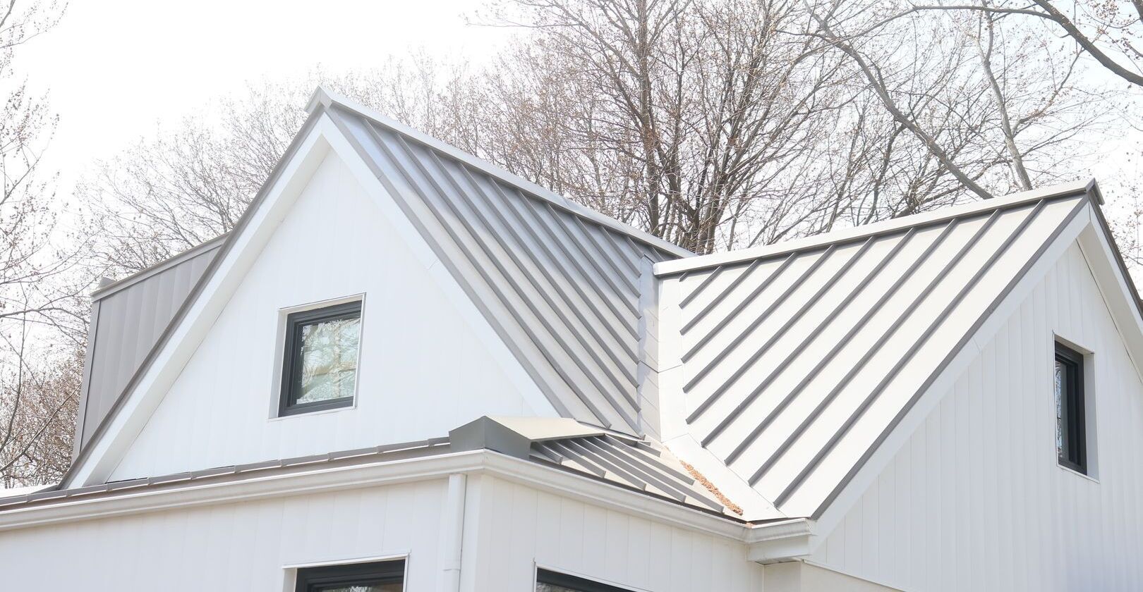 A white house with a metal roof and trees in the background.