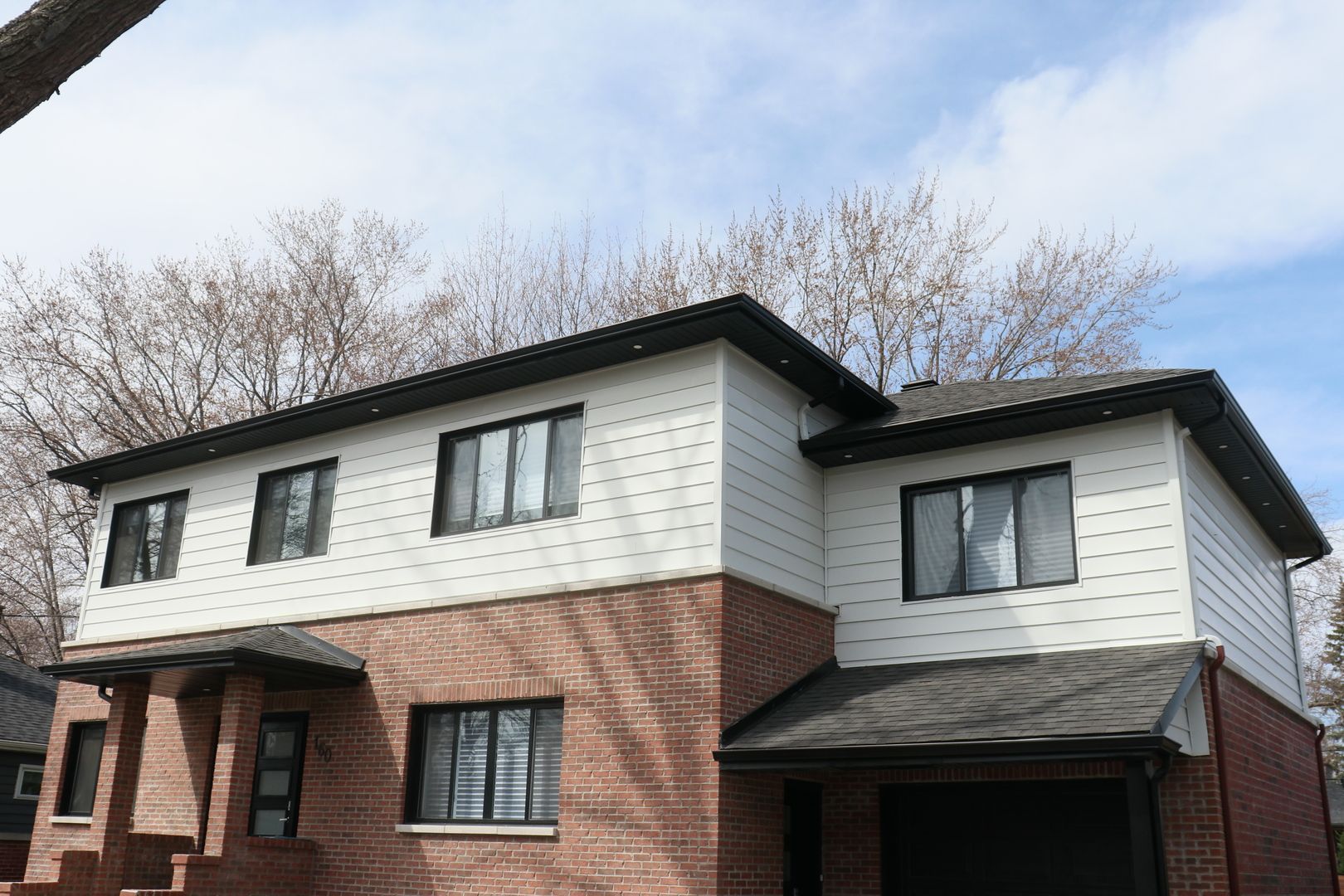Une maison en brique avec un revêtement blanc et des fenêtres noires