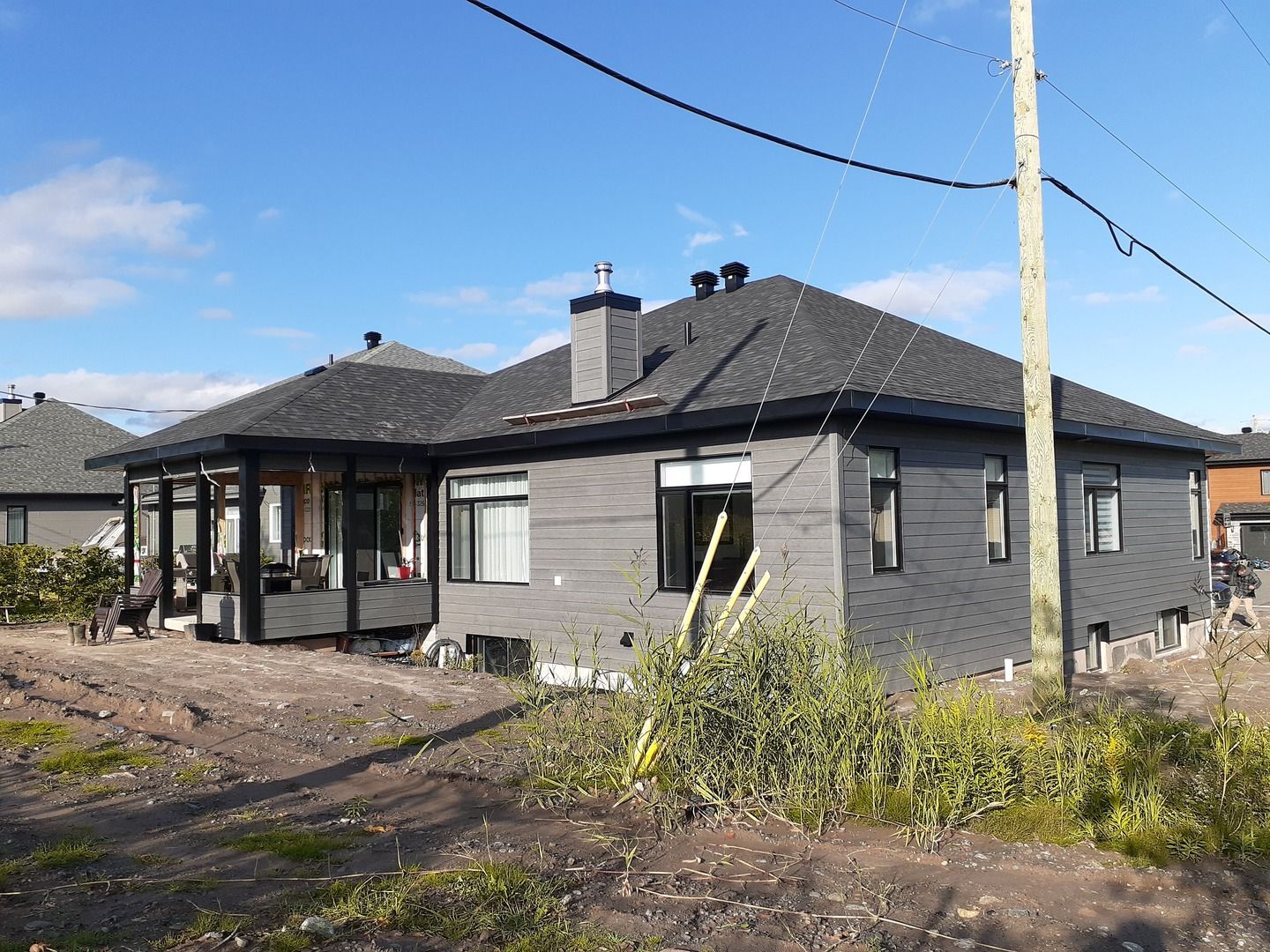 Une maison au toit noir se trouve au milieu d'un champ de terre.