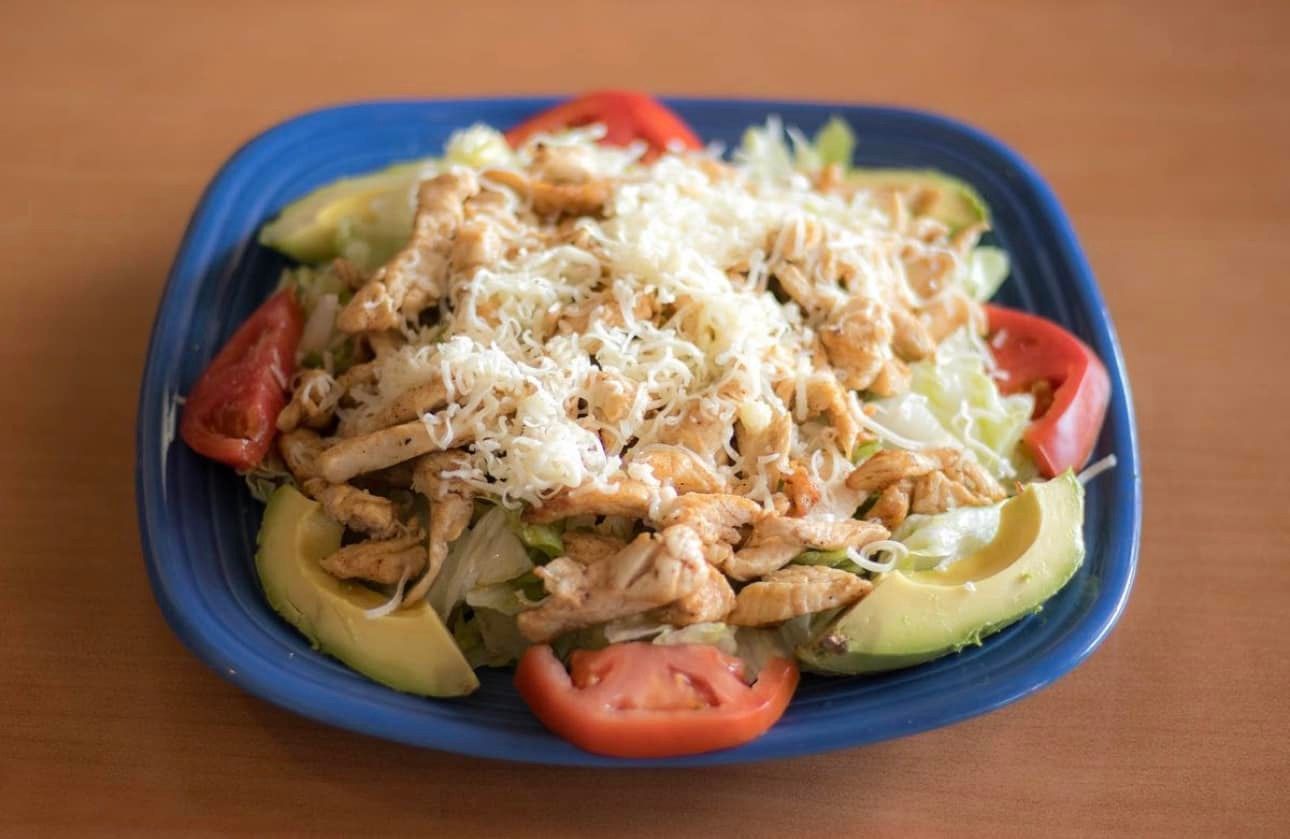 Chicken salad with avocado, tomato, and shredded cheese on a blue plate.