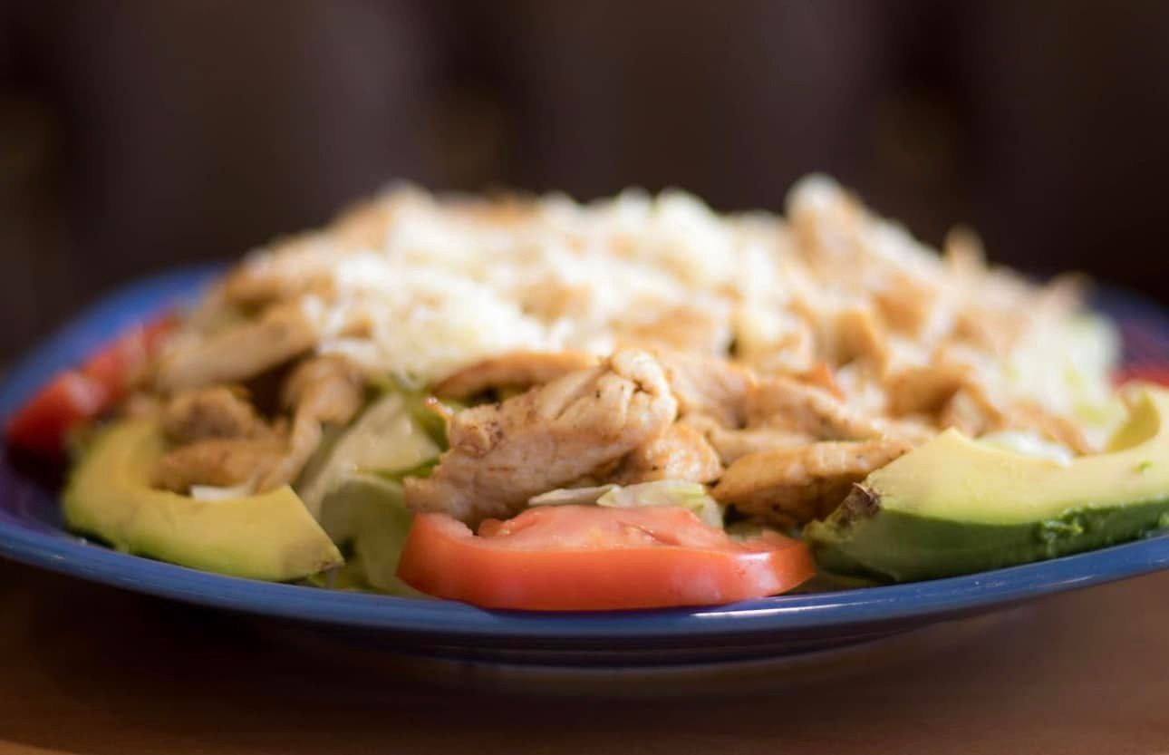 Chicken salad with avocado and tomato slices on a blue plate.