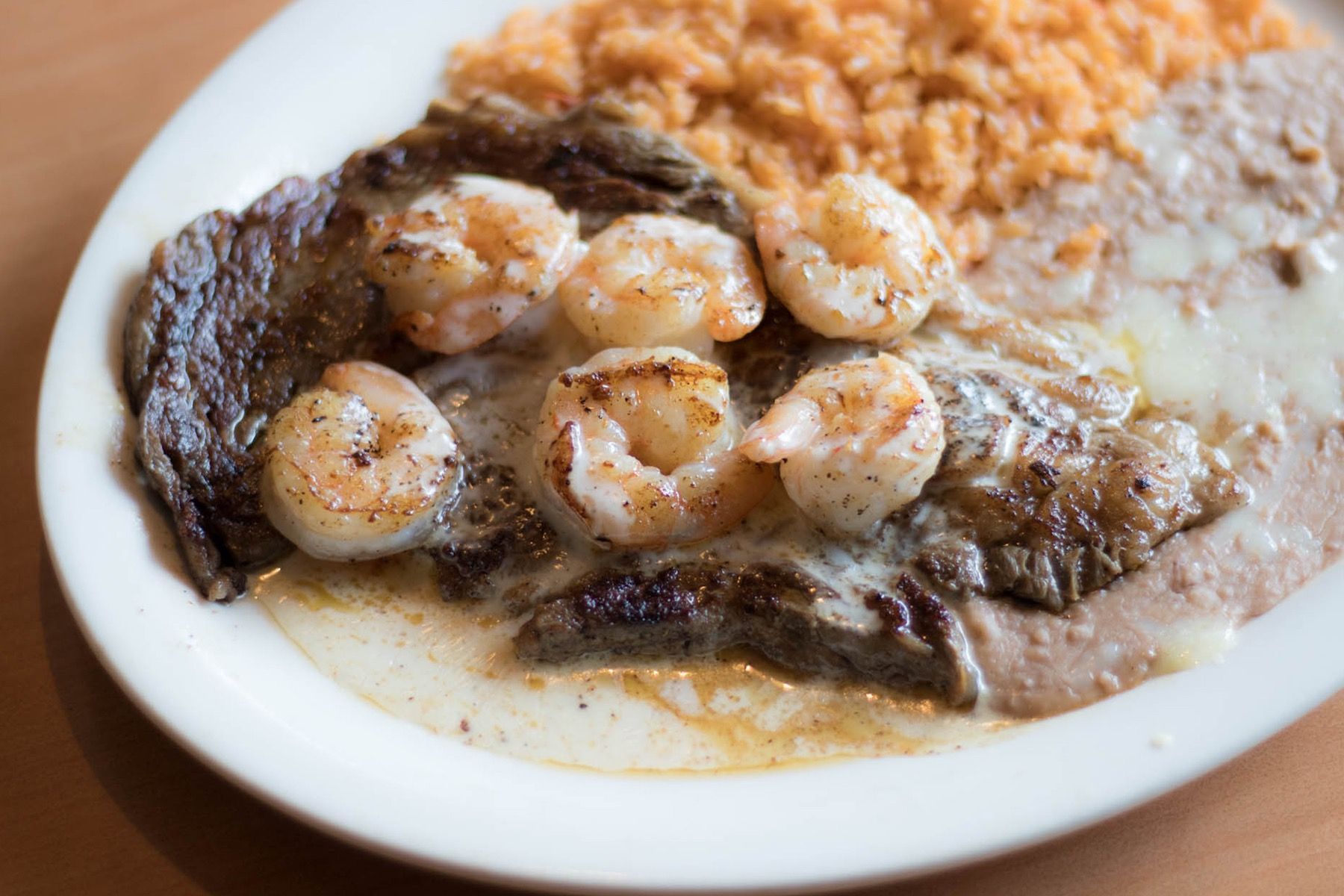 Steak and shrimp with rice and beans on a white plate.