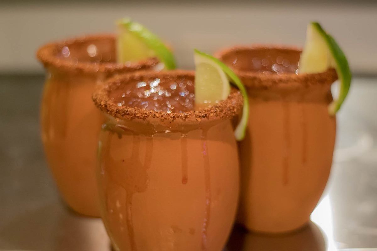 Three clay mugs, rimmed with spices, holding drinks, garnished with lime wedges.