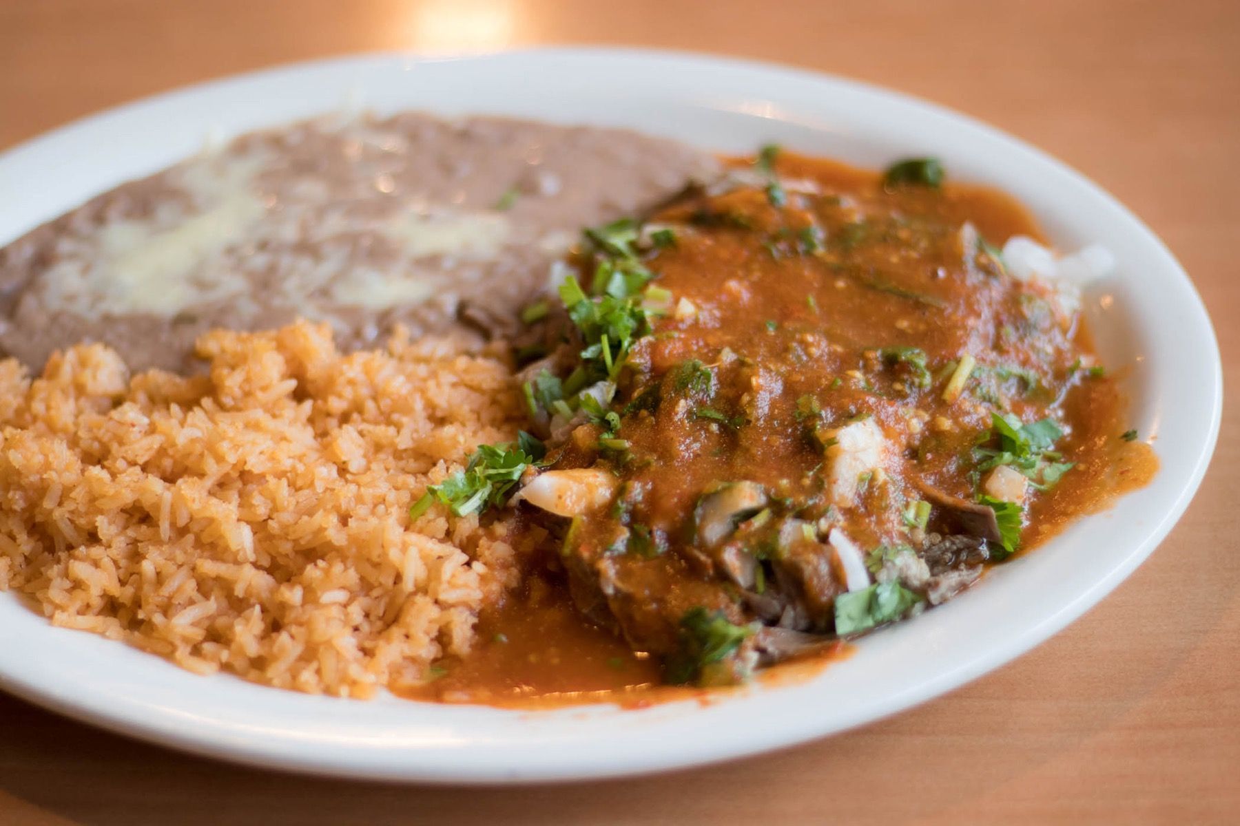 Plate of Mexican food: rice, refried beans, and enchilada with red sauce and cilantro.