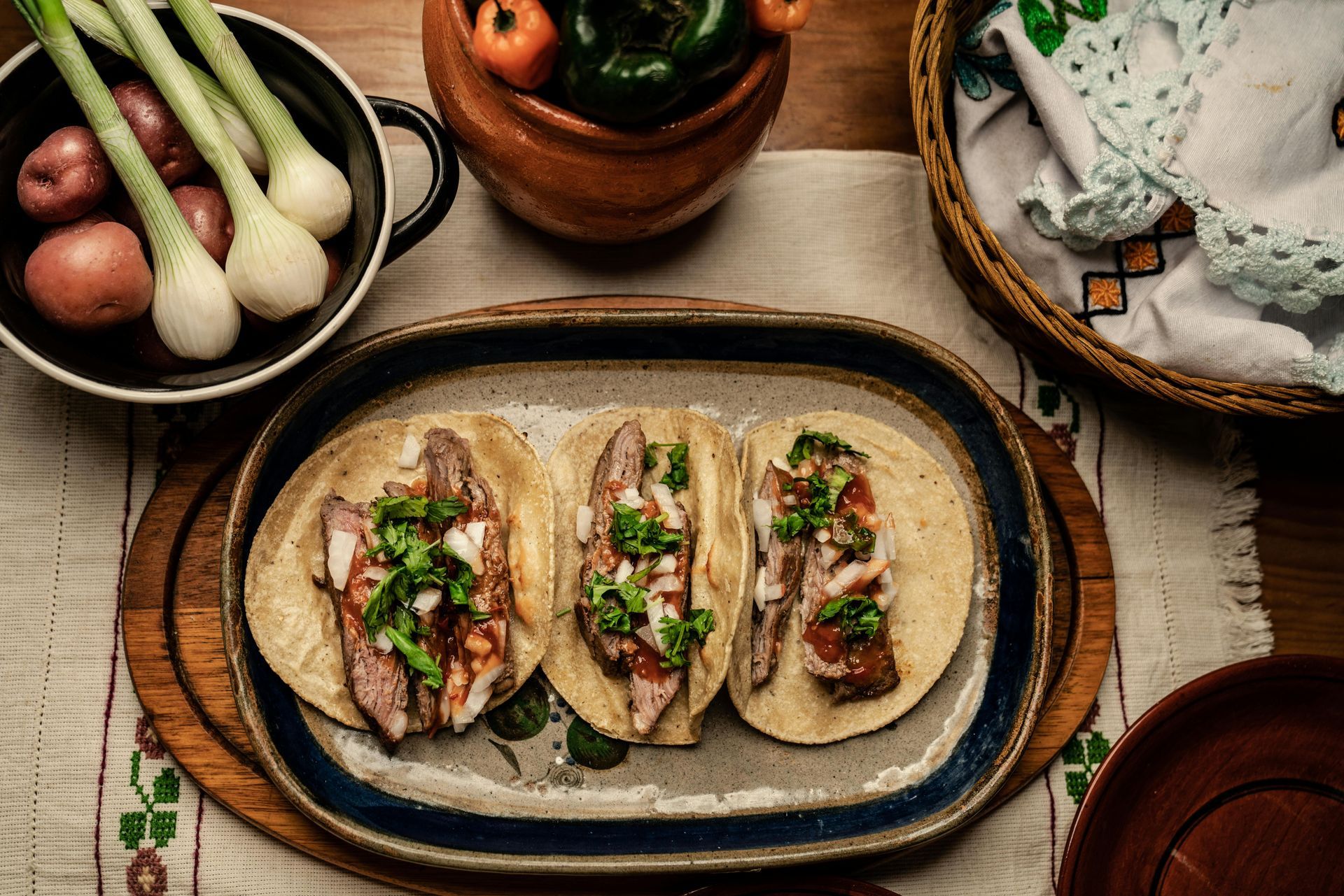 Three tacos on a plate, with onions, cilantro, and a side of vegetables.
