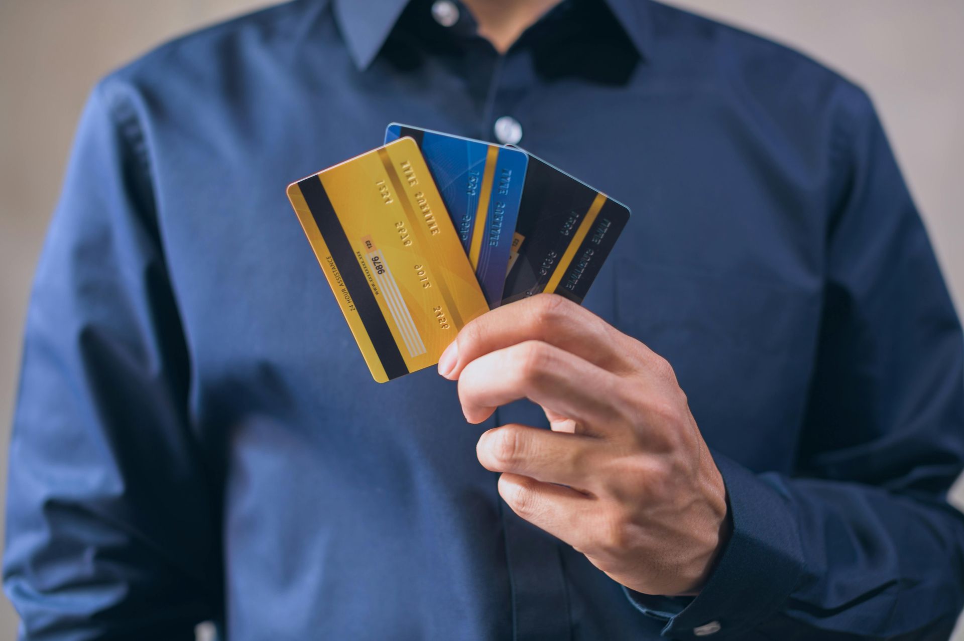 Man in blue shirt holding three credit cards, gold and blue.