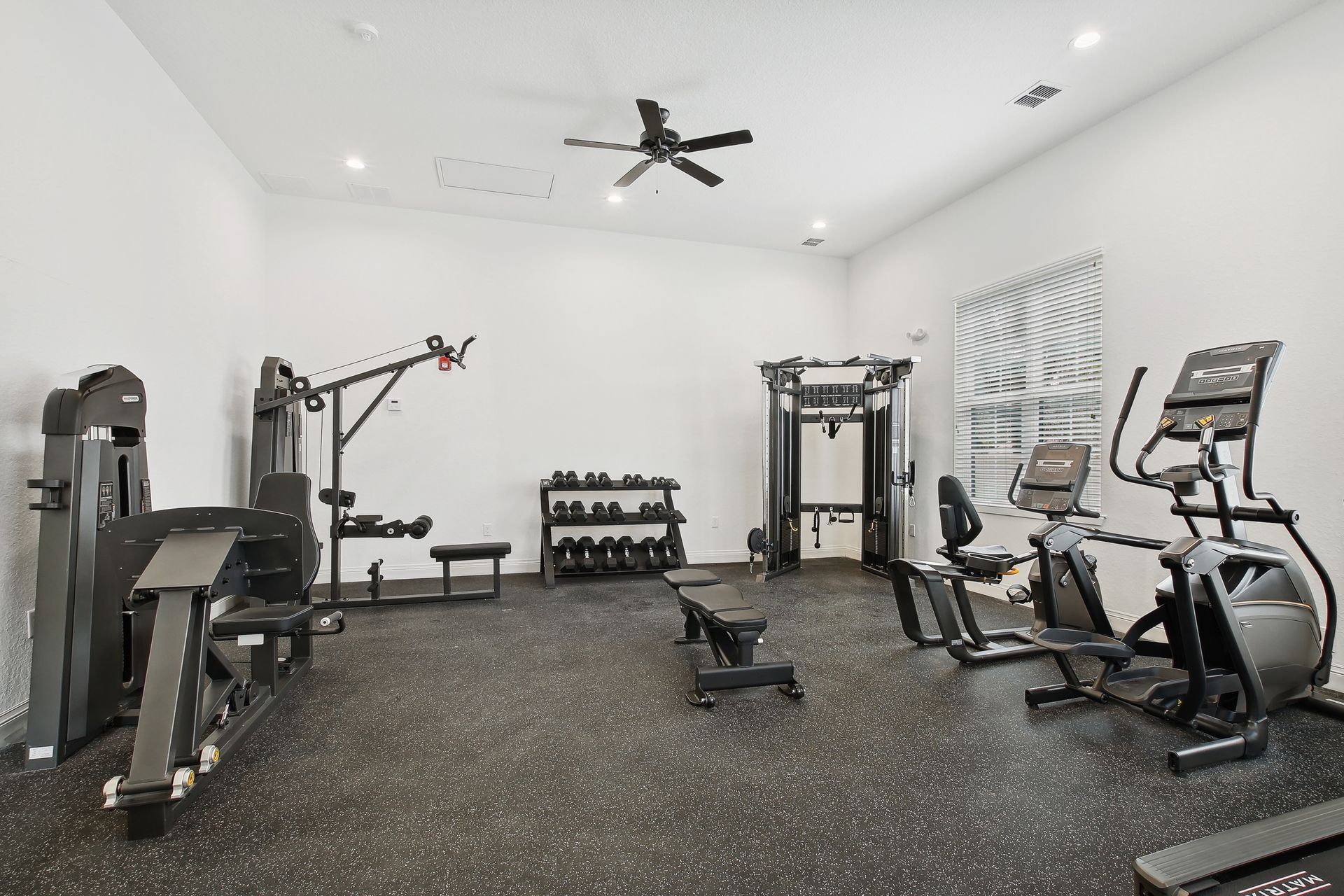 Home gym with black exercise equipment on a black speckled floor.