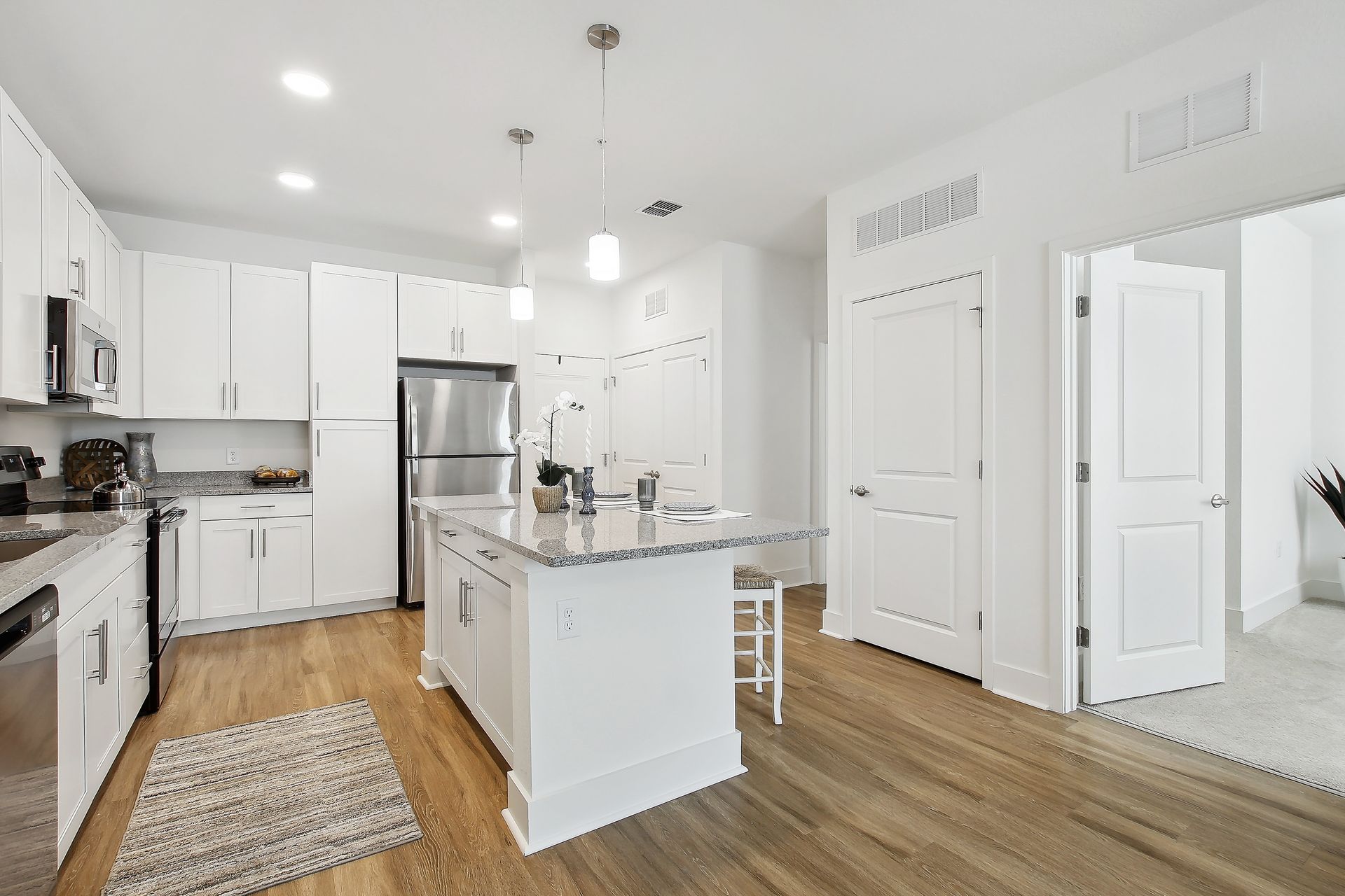 Bright white kitchen with stainless steel appliances and island. Wood floor and door to other room.