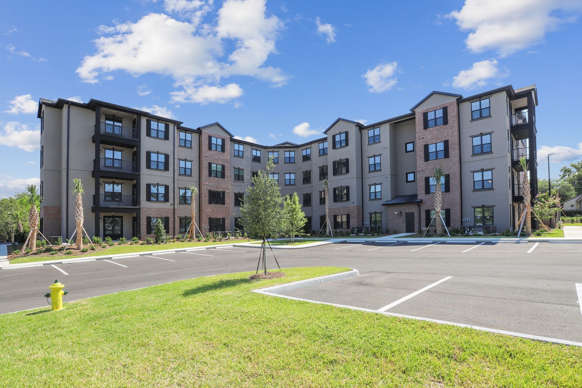Multi-story apartment building with parking, green lawn, and a blue sky.