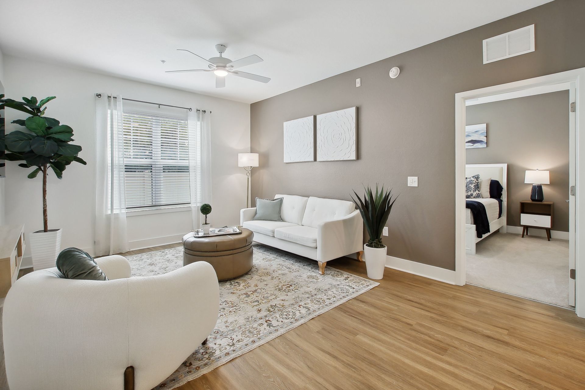 Living room with white furniture, neutral walls, rug, open doorway to bedroom.
