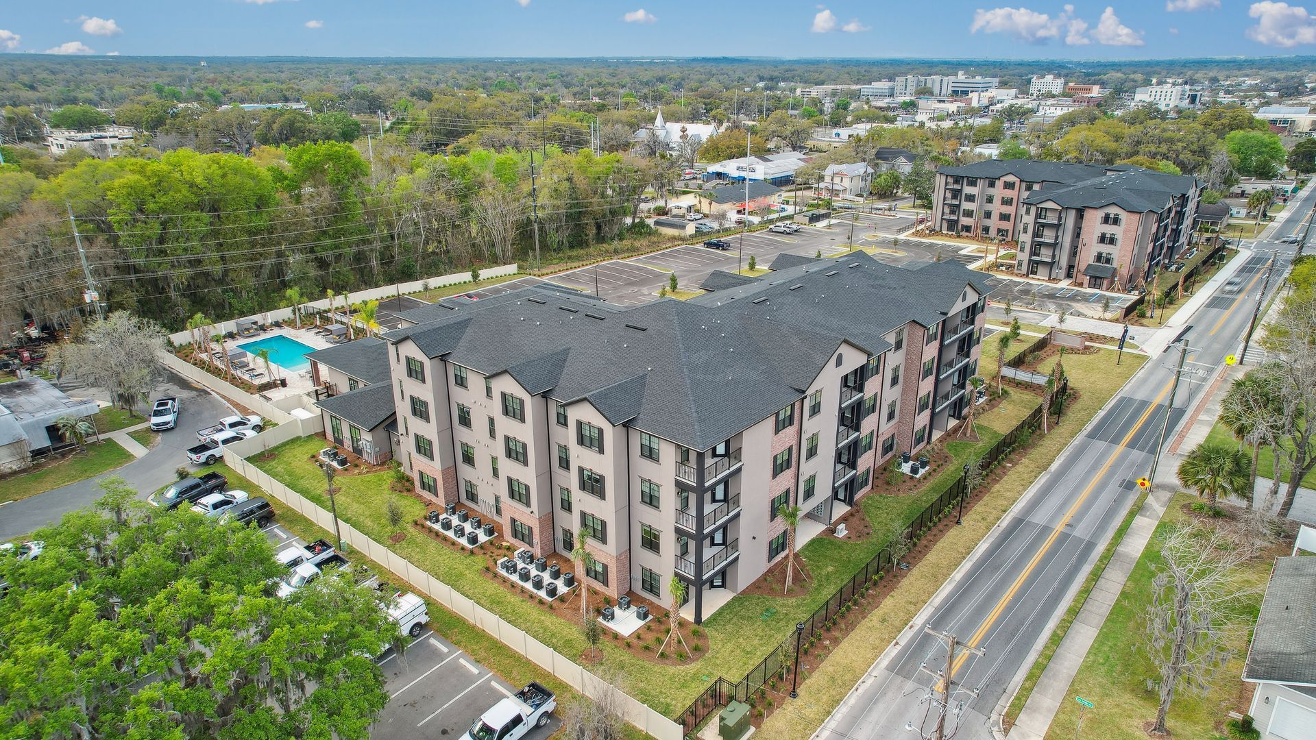 Aerial view of a multi-story apartment building, with a pool and surrounding neighborhood in background.