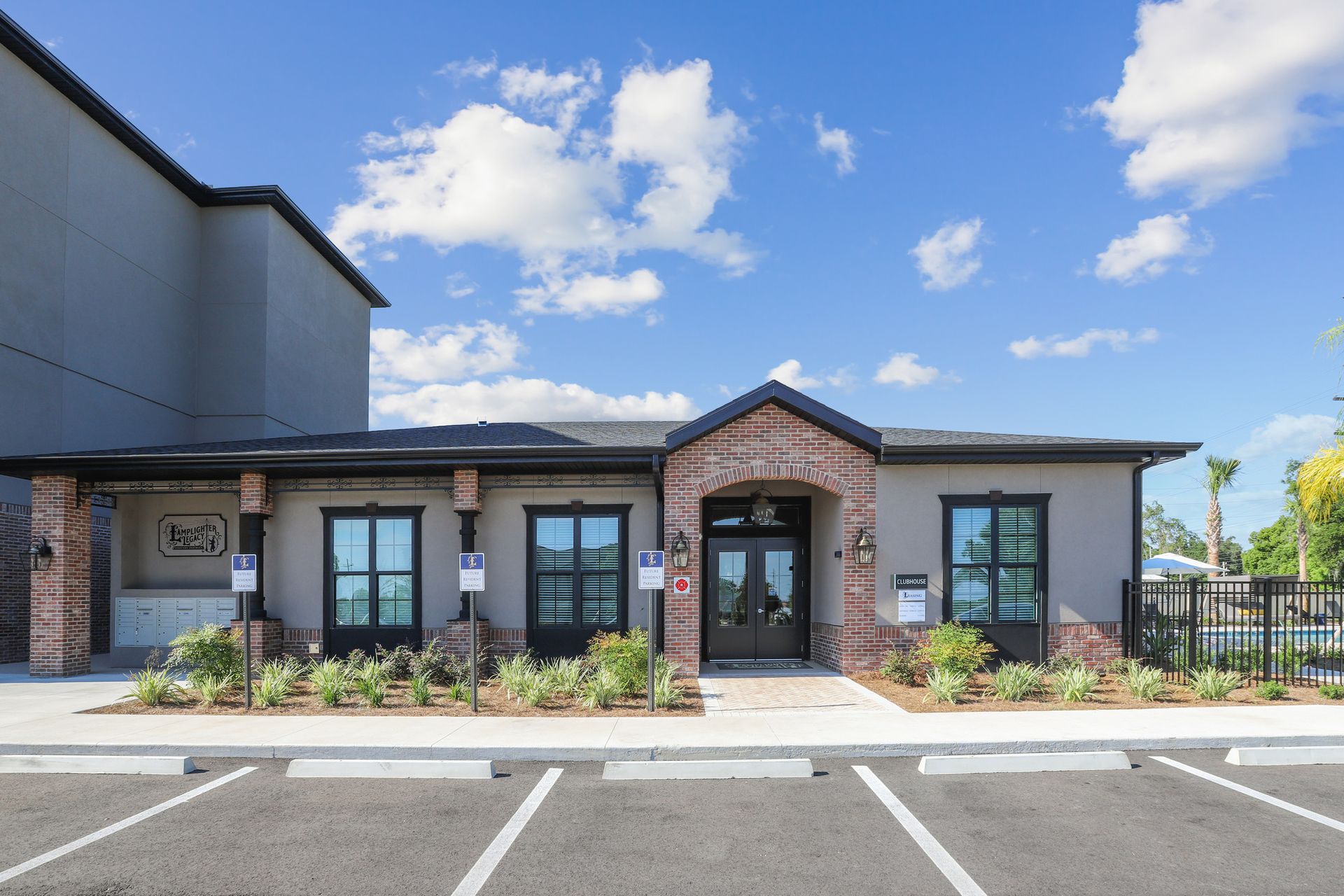 Apartment leasing office with brick accents, windows, parking spaces, and a blue sky.