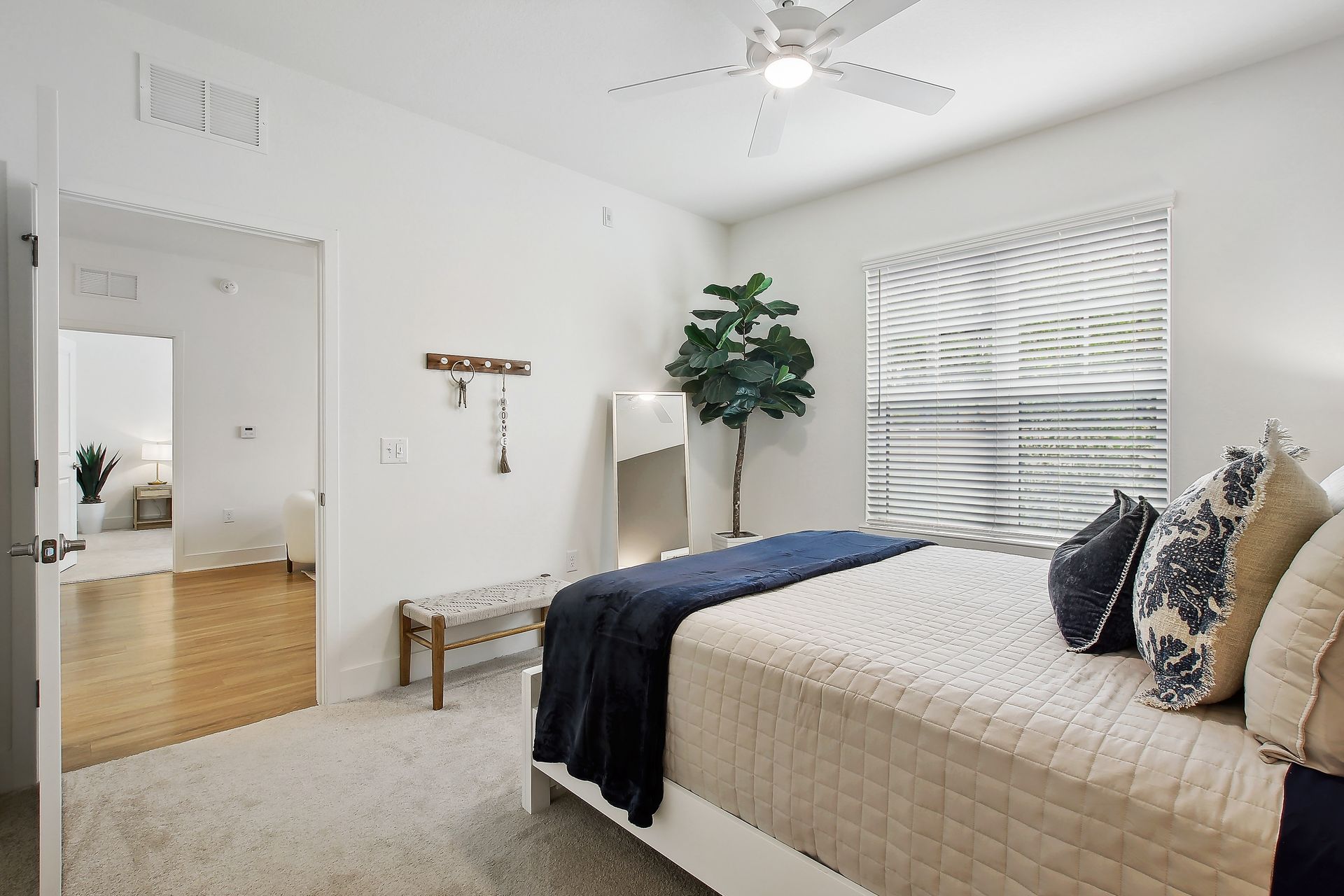 Bedroom with a bed, mirror, bench, and a large plant, bathed in natural light.
