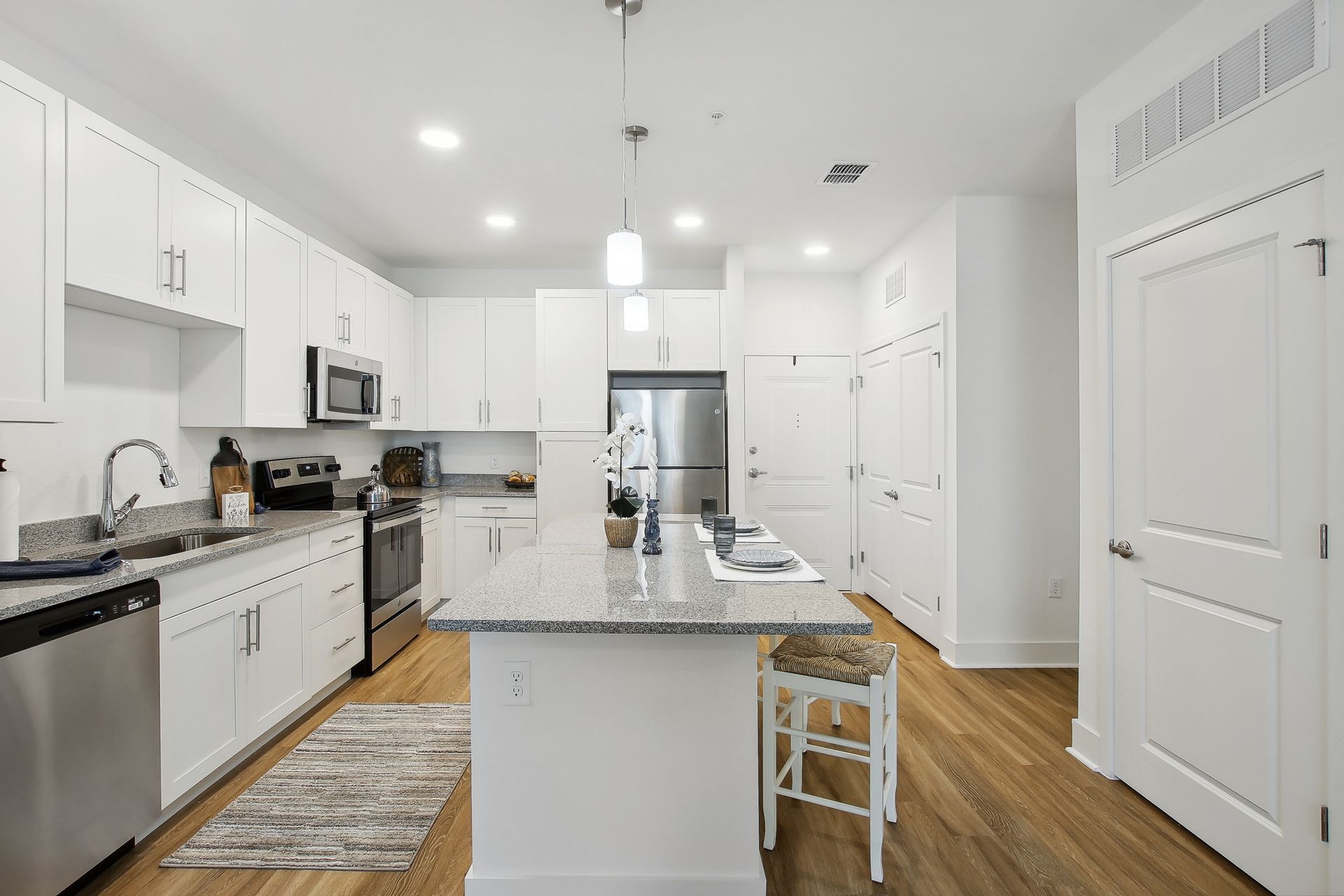 Bright white kitchen with stainless steel appliances, island with granite countertop, and hardwood floors.