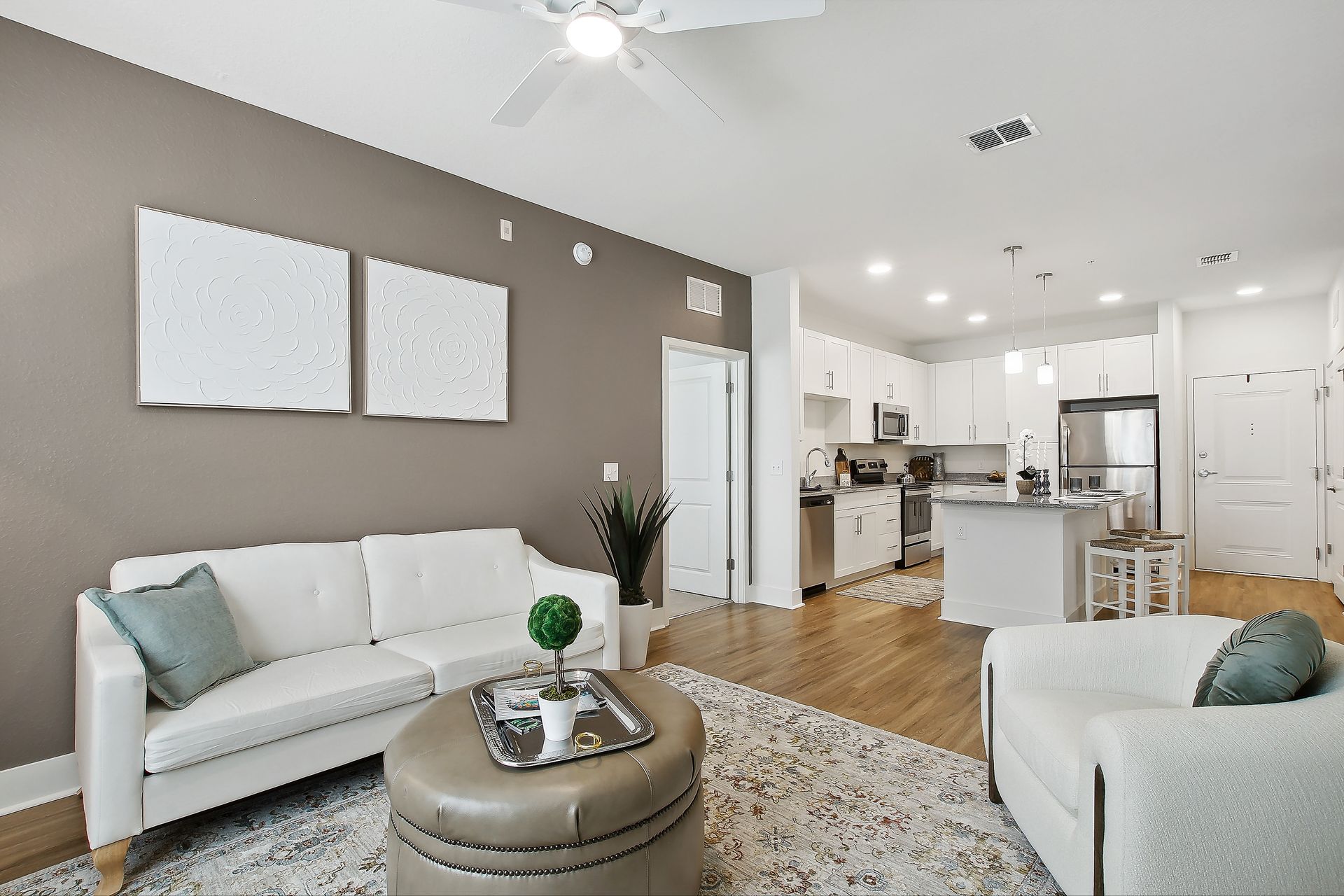 Living room with white furniture, gray wall, open kitchen, and wooden floors.