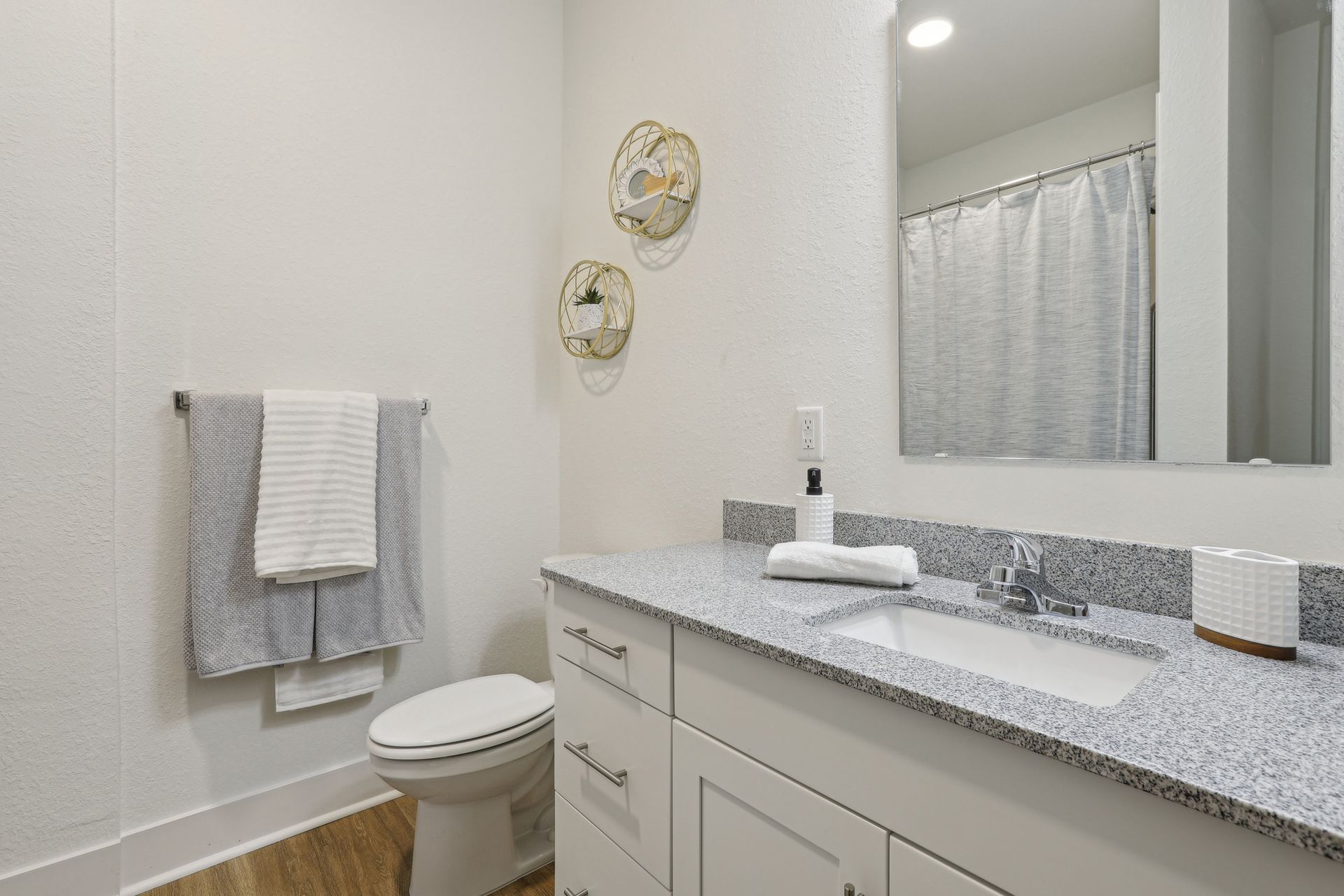 Bathroom with white cabinets, granite countertop, and toilet. Towels on bar; gold wall art.