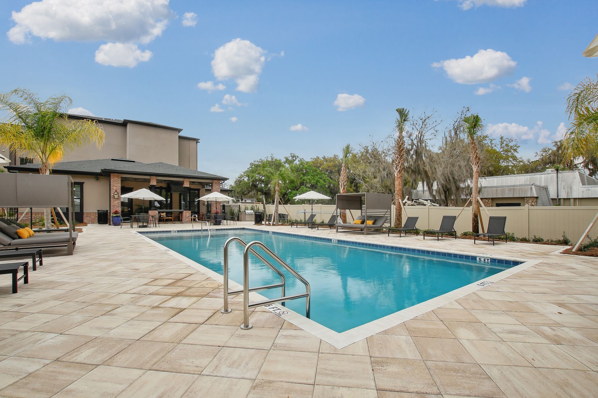 Swimming pool with lounge chairs, umbrellas, and building under a blue sky.