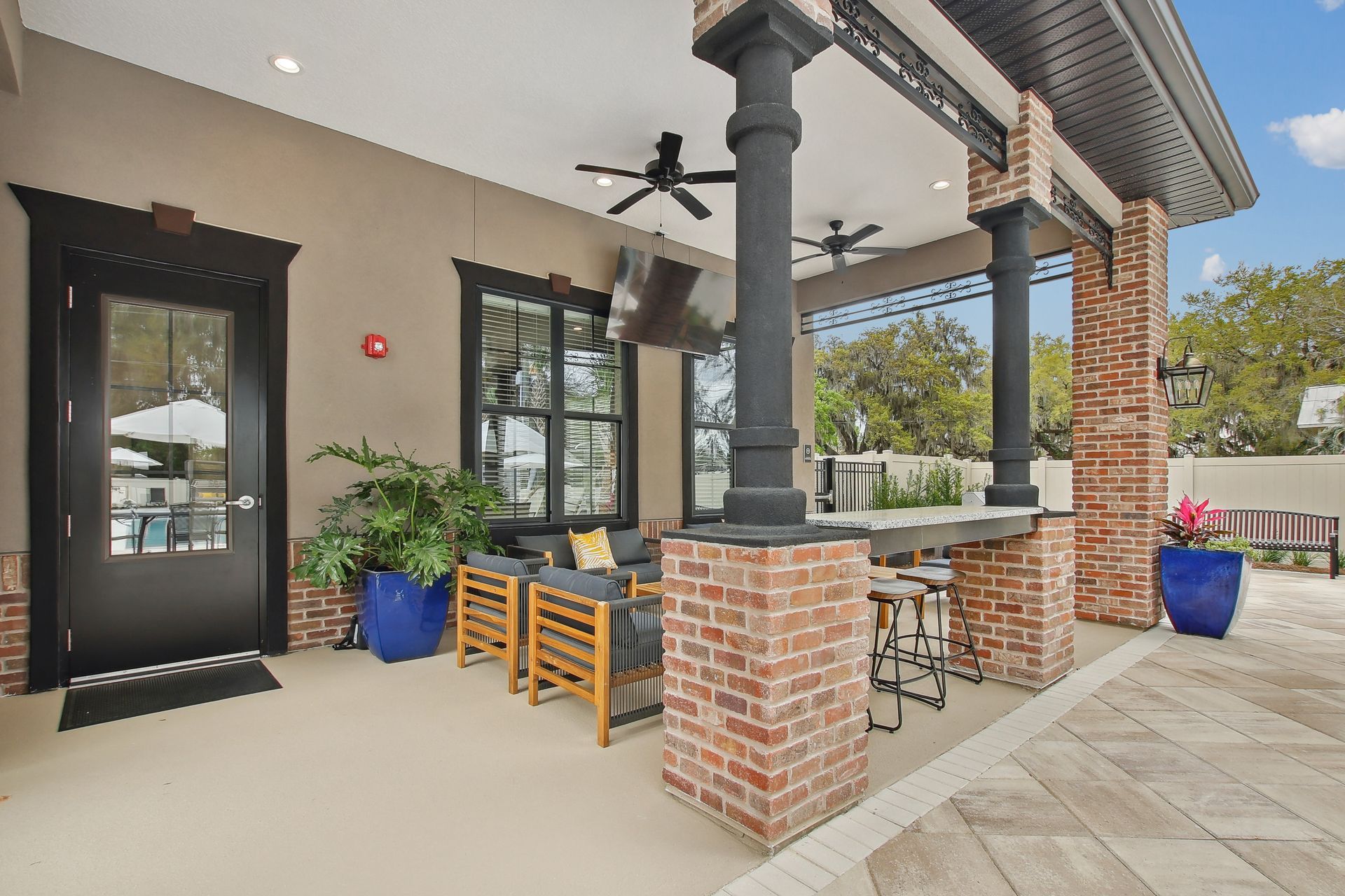 Outdoor patio with brick columns, seating, bar, and ceiling fans; next to door and windows.