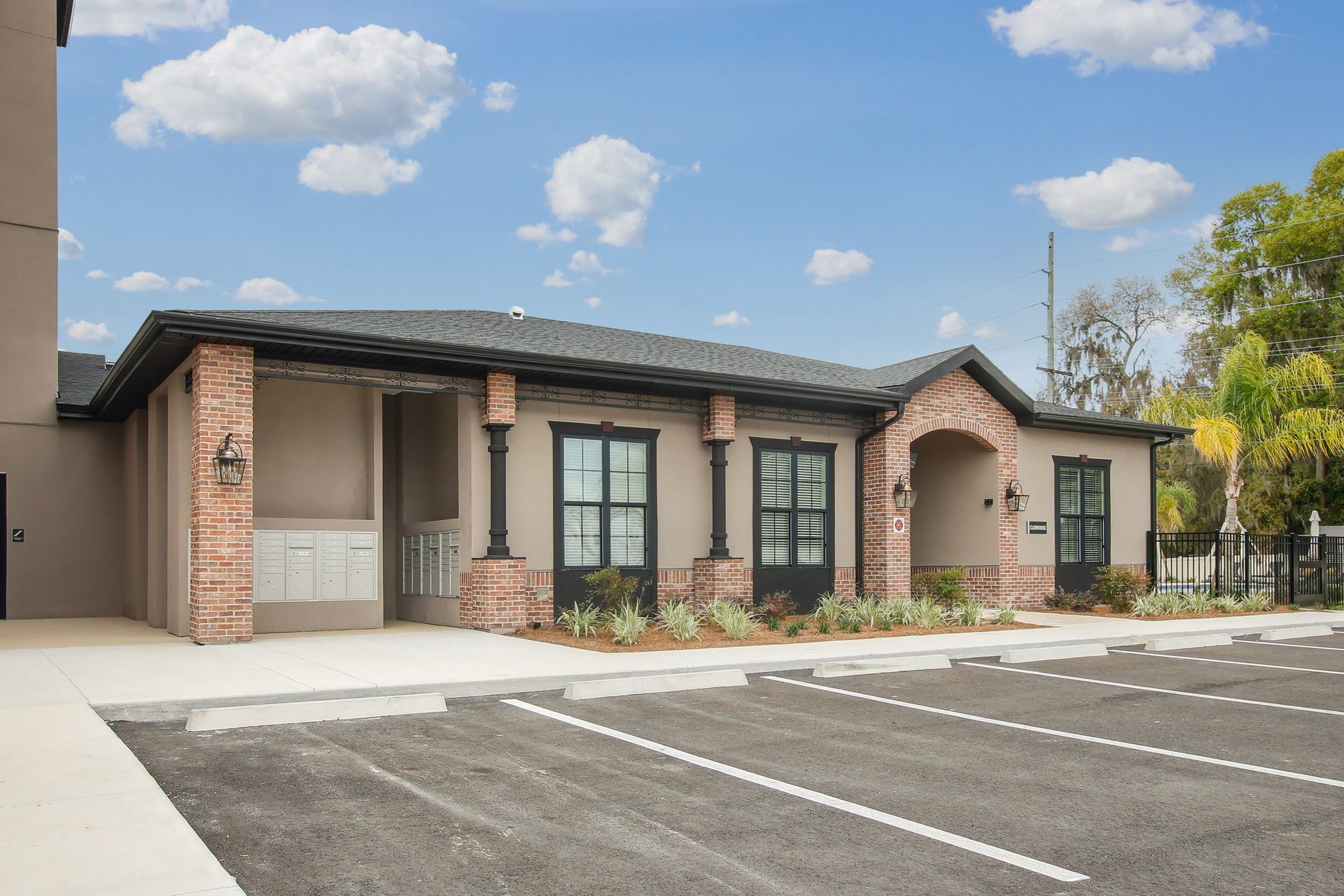 Exterior of a light brown and brick building with a black roof. Parking lot in front, blue sky.