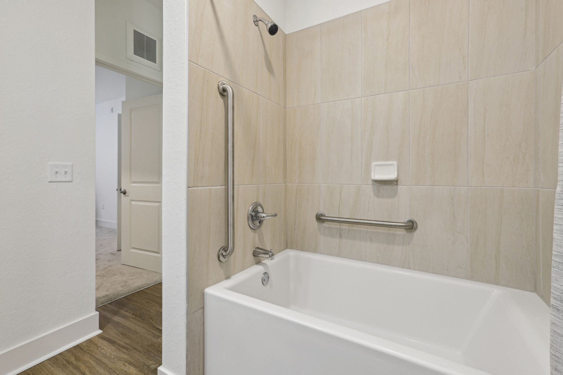 Bathroom with a white bathtub, beige tiled walls, and grab bars for accessibility.