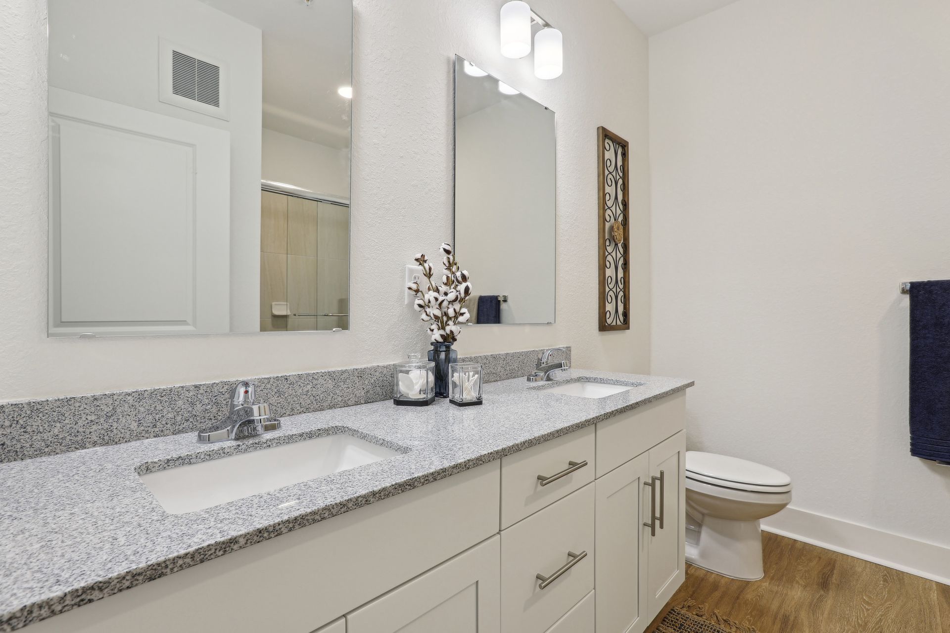 Bathroom with double sinks, light gray countertop, white cabinets, and two mirrors.