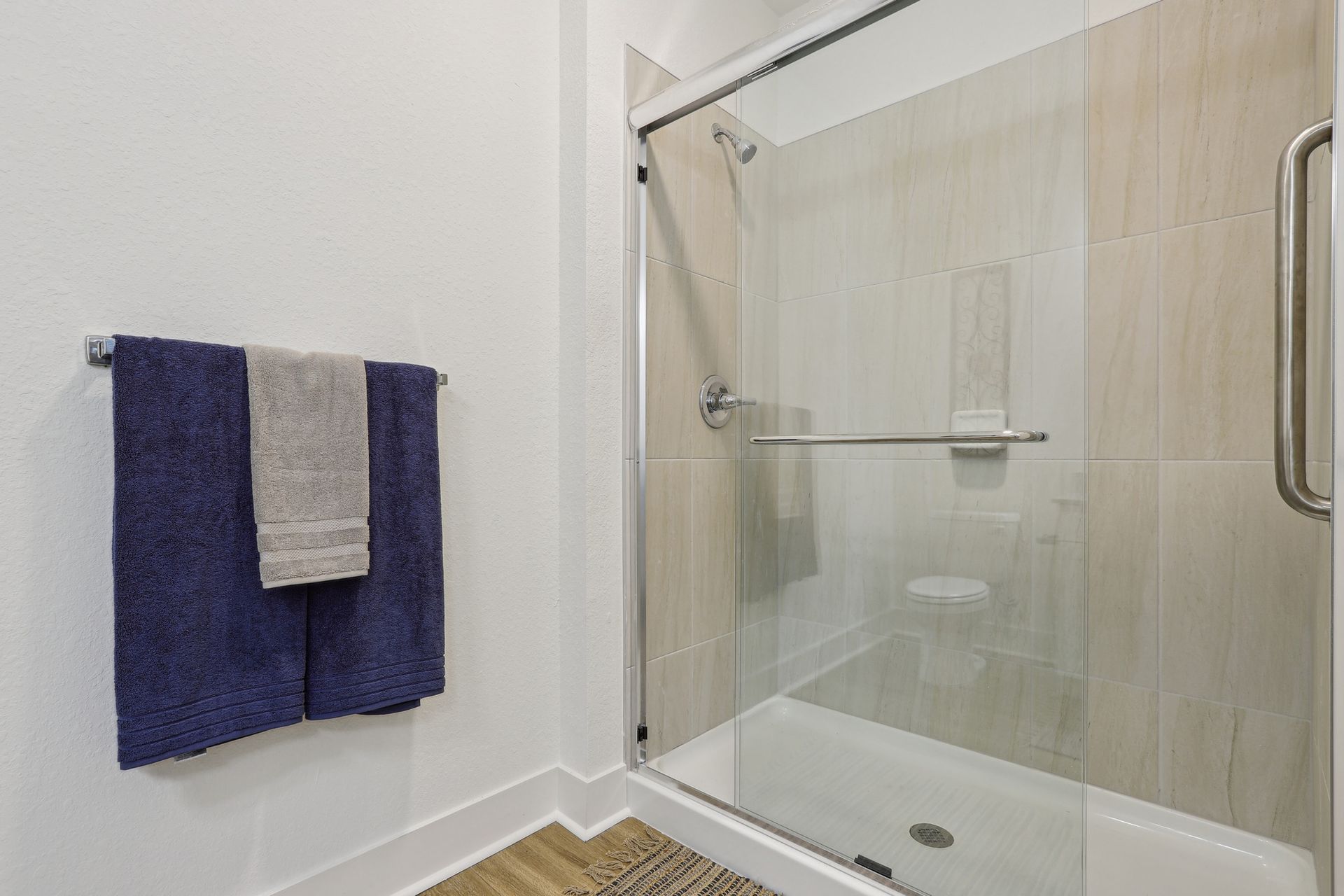 Bathroom with a glass shower, beige tiles, and towels on a rack.