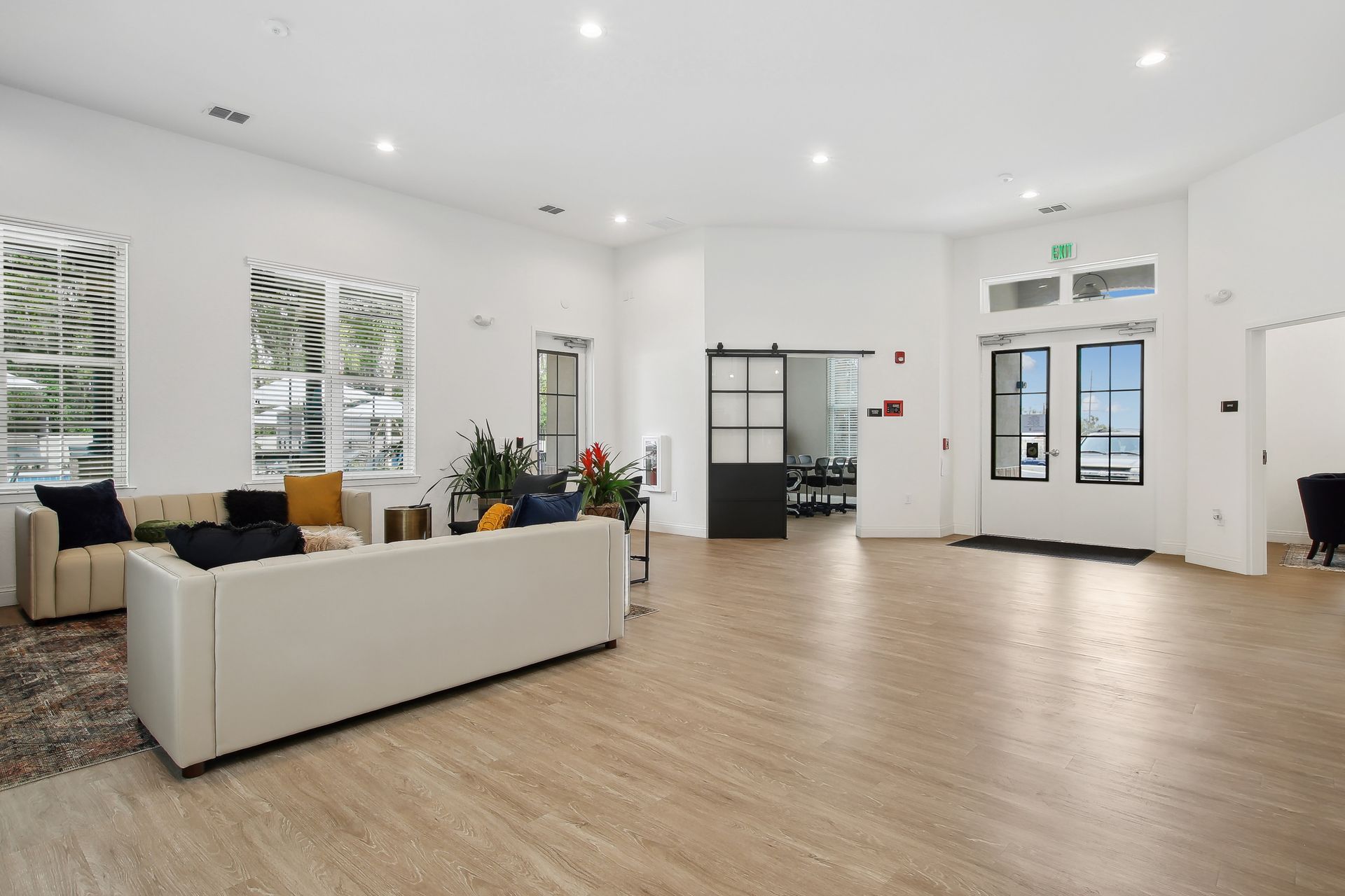 Spacious, bright room with light wood flooring, a white couch, and a large entrance door.