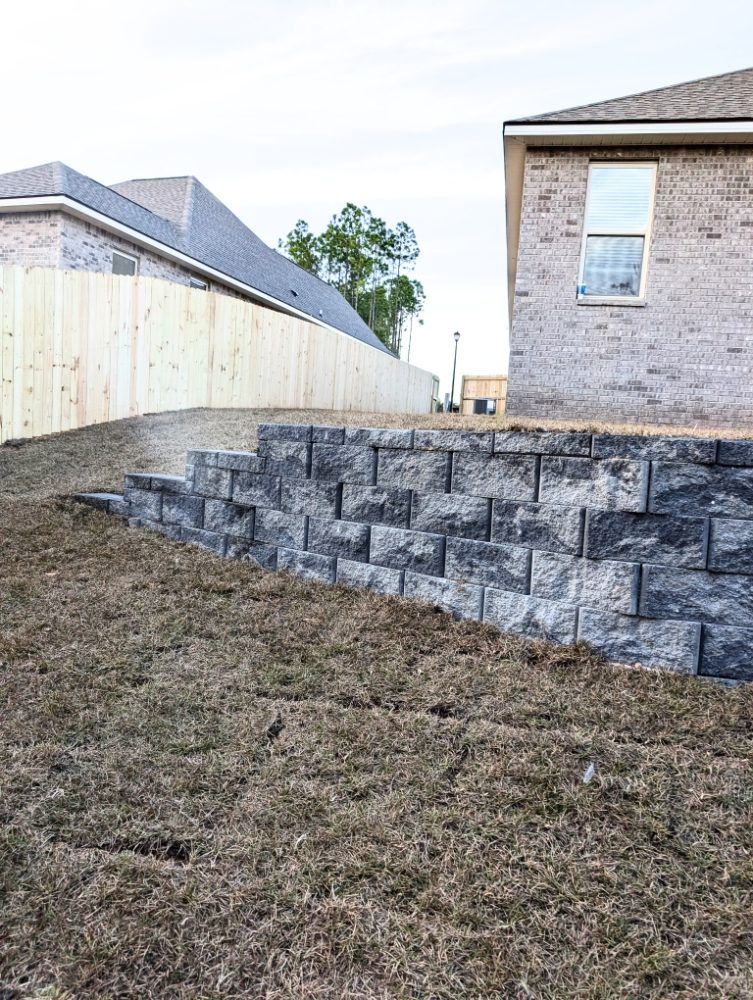 Backyard with a stacked stone retaining wall beside a brick house and fenced yard