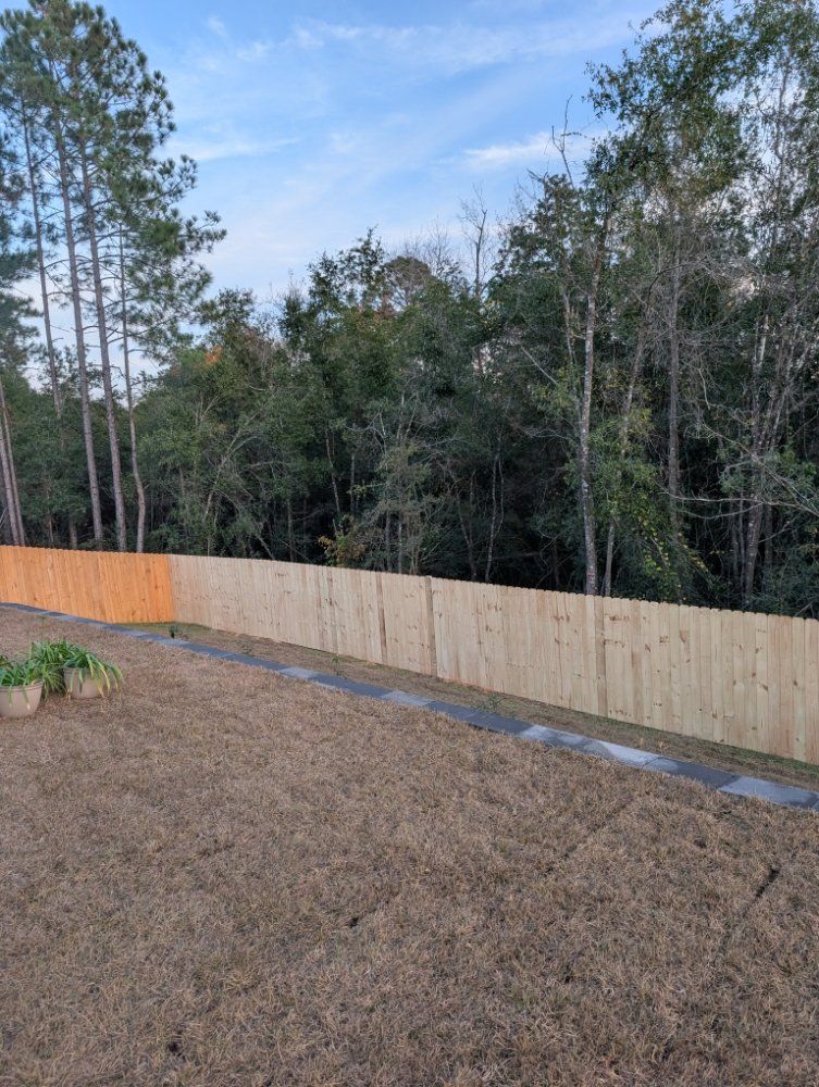 New wooden privacy fence along a grassy yard beside trees and a blue sky