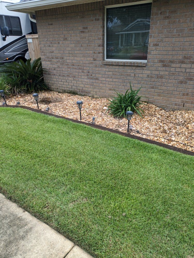 Front yard with a brick house wall, green lawn, and a mulched garden bed with small solar lights.